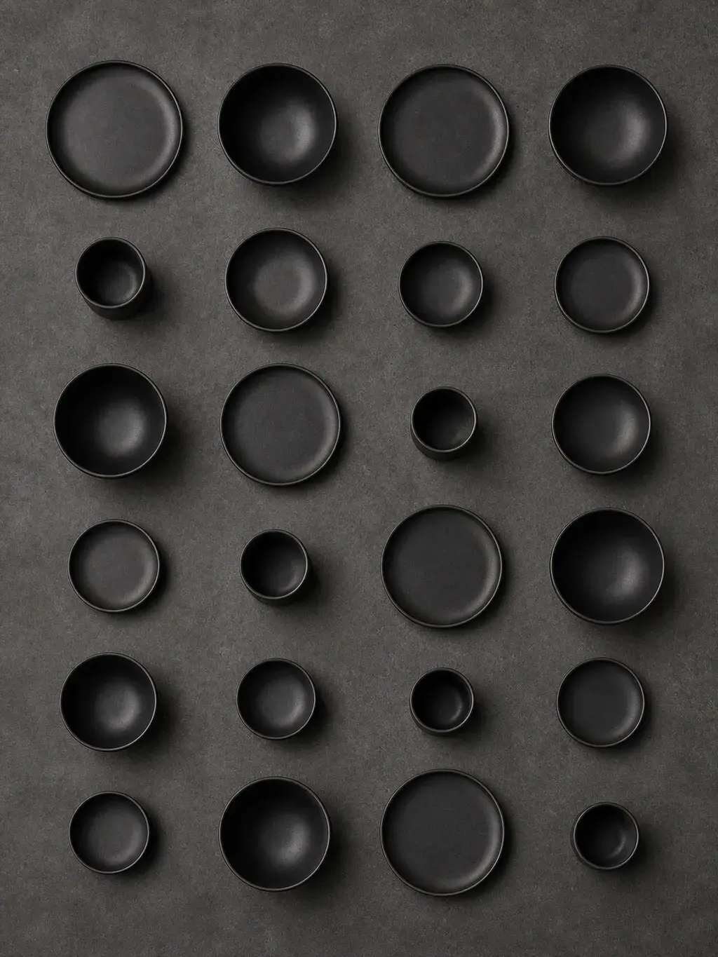 Flat lay de bols et assiettes en céramique noire sur béton gris