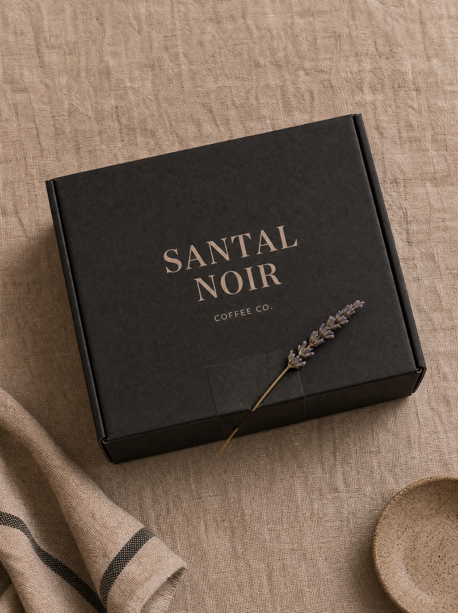 Boîte cadeau noire fermée avec branche lavande – nappe lin rayée, cuillère bois, composition épurée