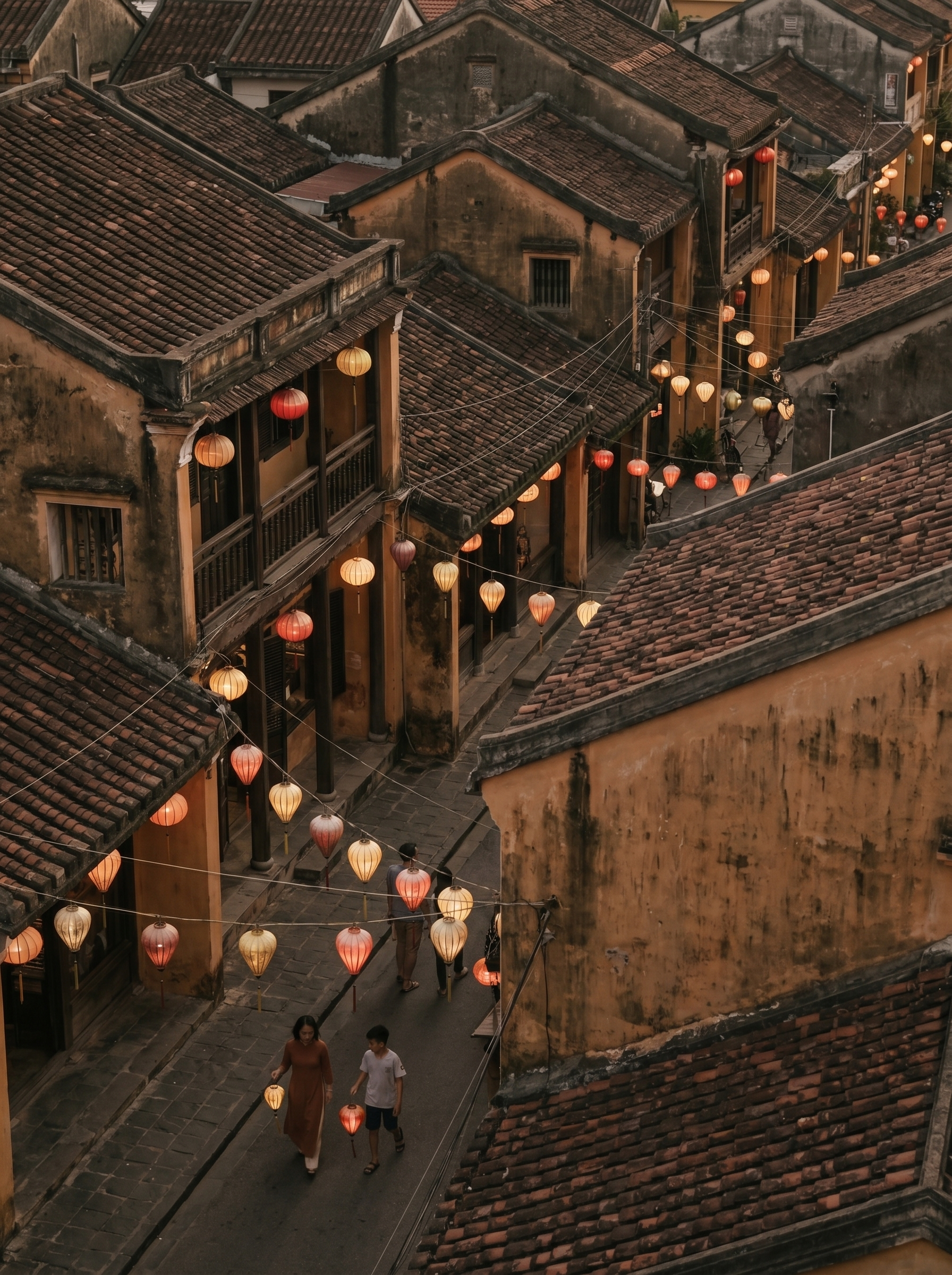 Vue aérienne sur toits et ruelles de la vieille ville de Hội An avec lanternes colorées allumées et deux silhouettes au sol