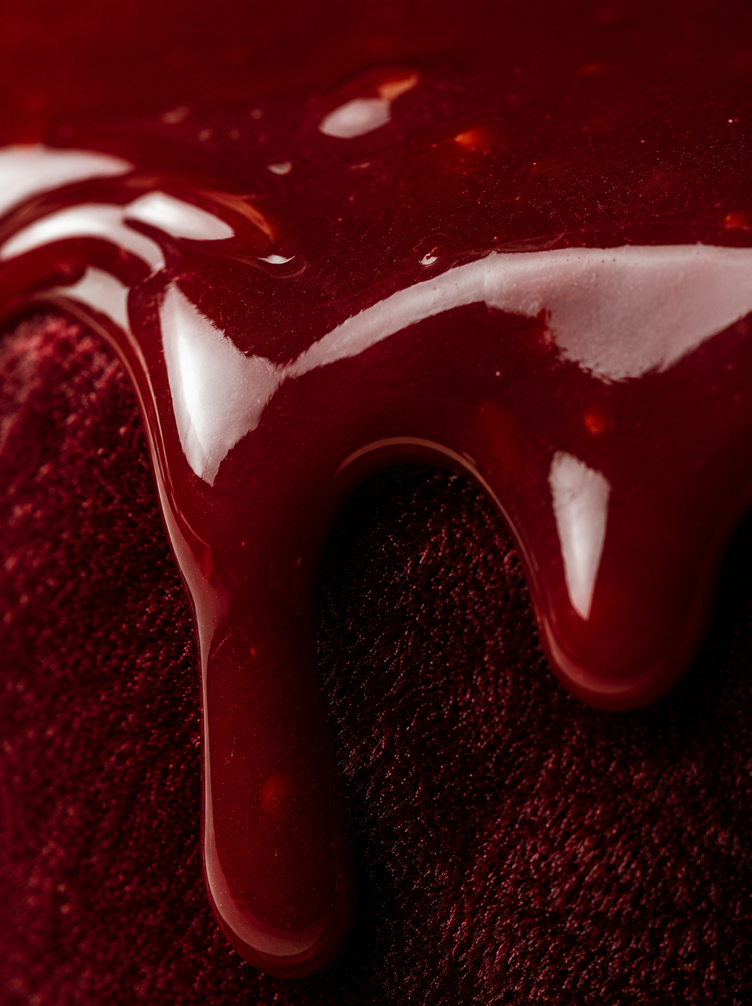 Macro glaçage miroir bordeaux coulant sur velours rouge – reflets brillants, fond rouge profond