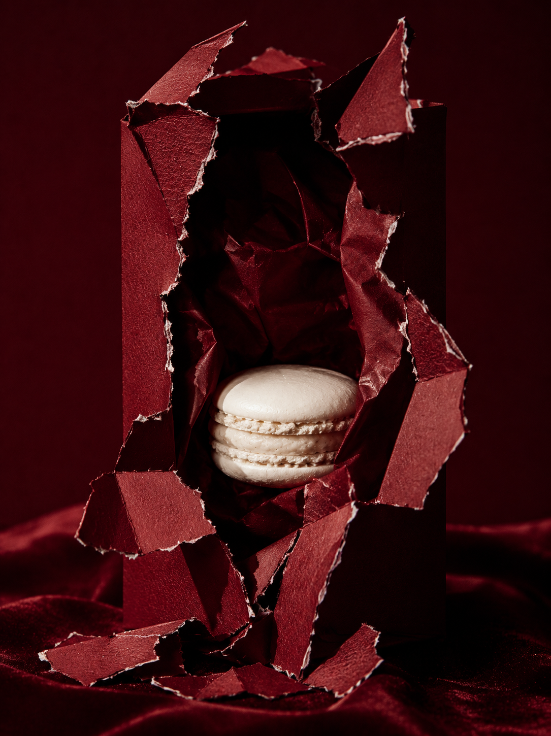 Macaron blanc jaillissant d'une boîte pâtisserie bordeaux déchirée – fond velours, packaging