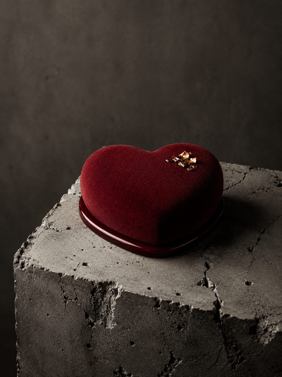 Entremets cœur velours rouge bordeaux sur bloc béton – éclats feuille d'or, fond gris sombre