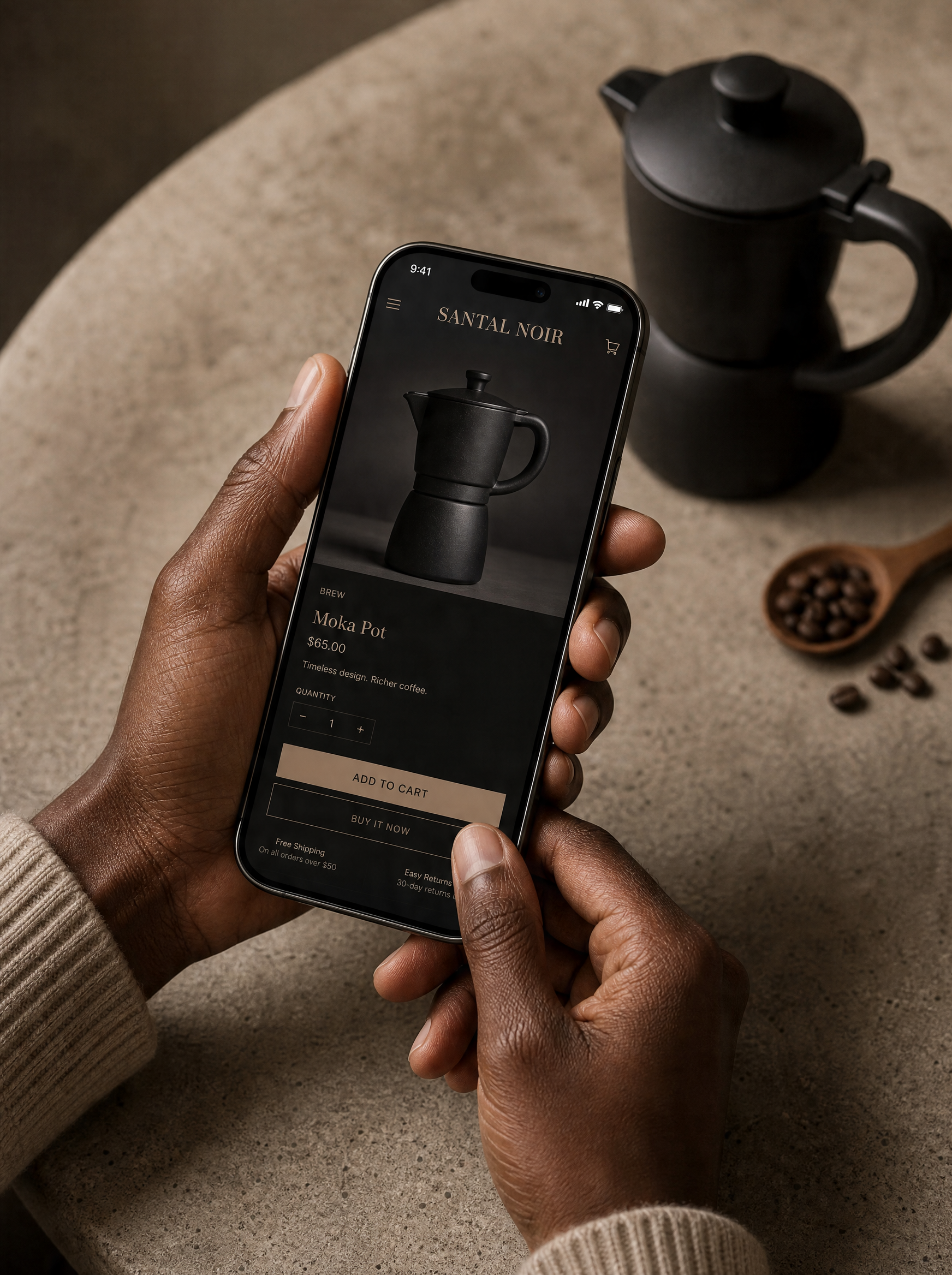 Mains tenant smartphone montrant page boutique cafetière moka – table béton, grains, cuillère bois