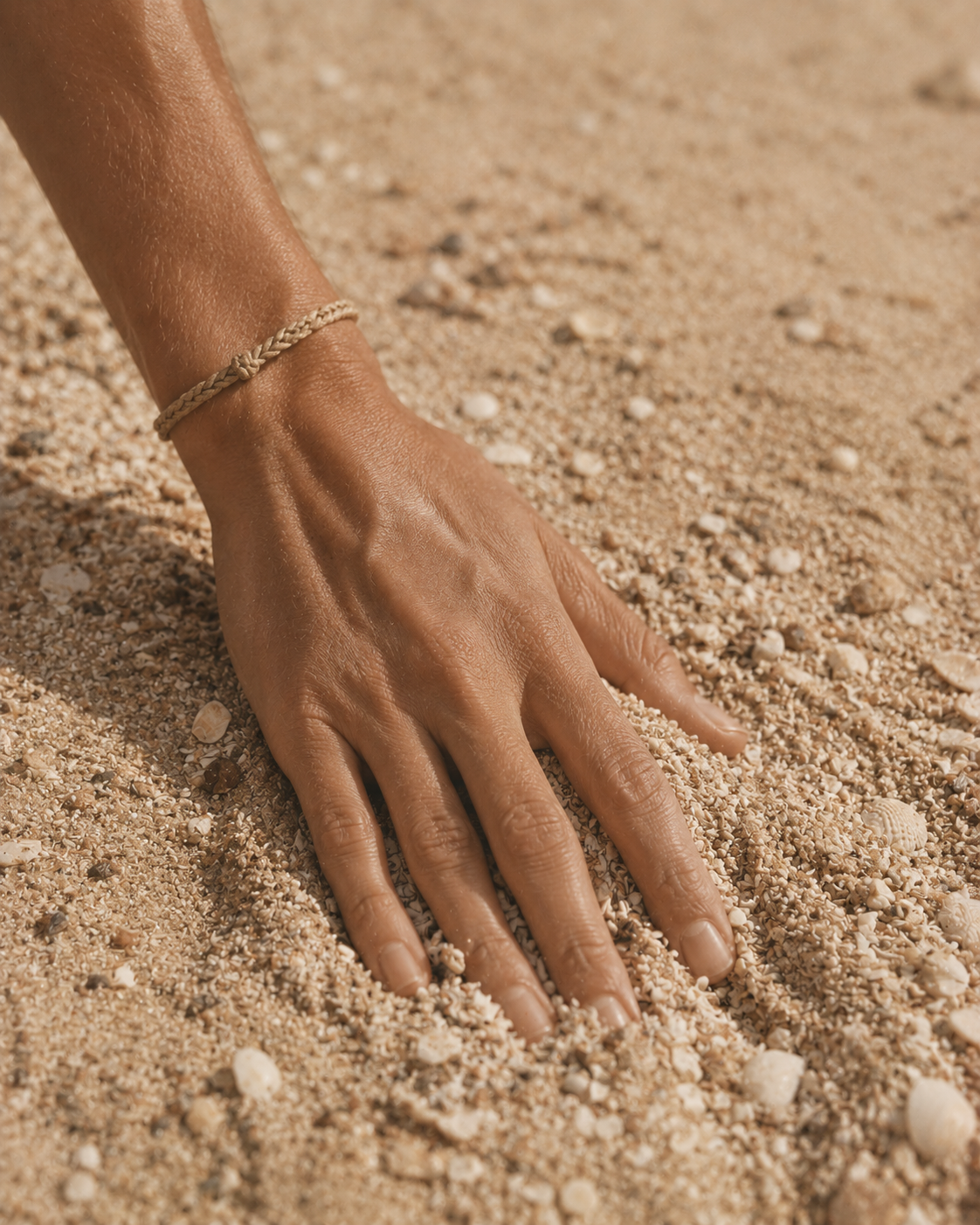 Main posée sur sable fin avec bracelet tressé – gros plan plage sensuelle