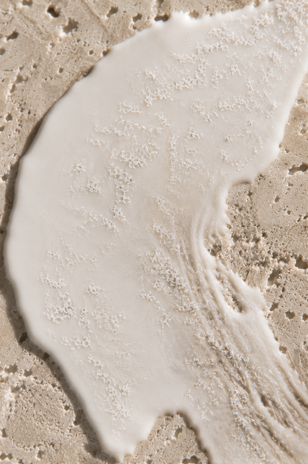 Vue de dessus crème blanche étalée sur travertin – microparticules, texture minérale, lumière douce