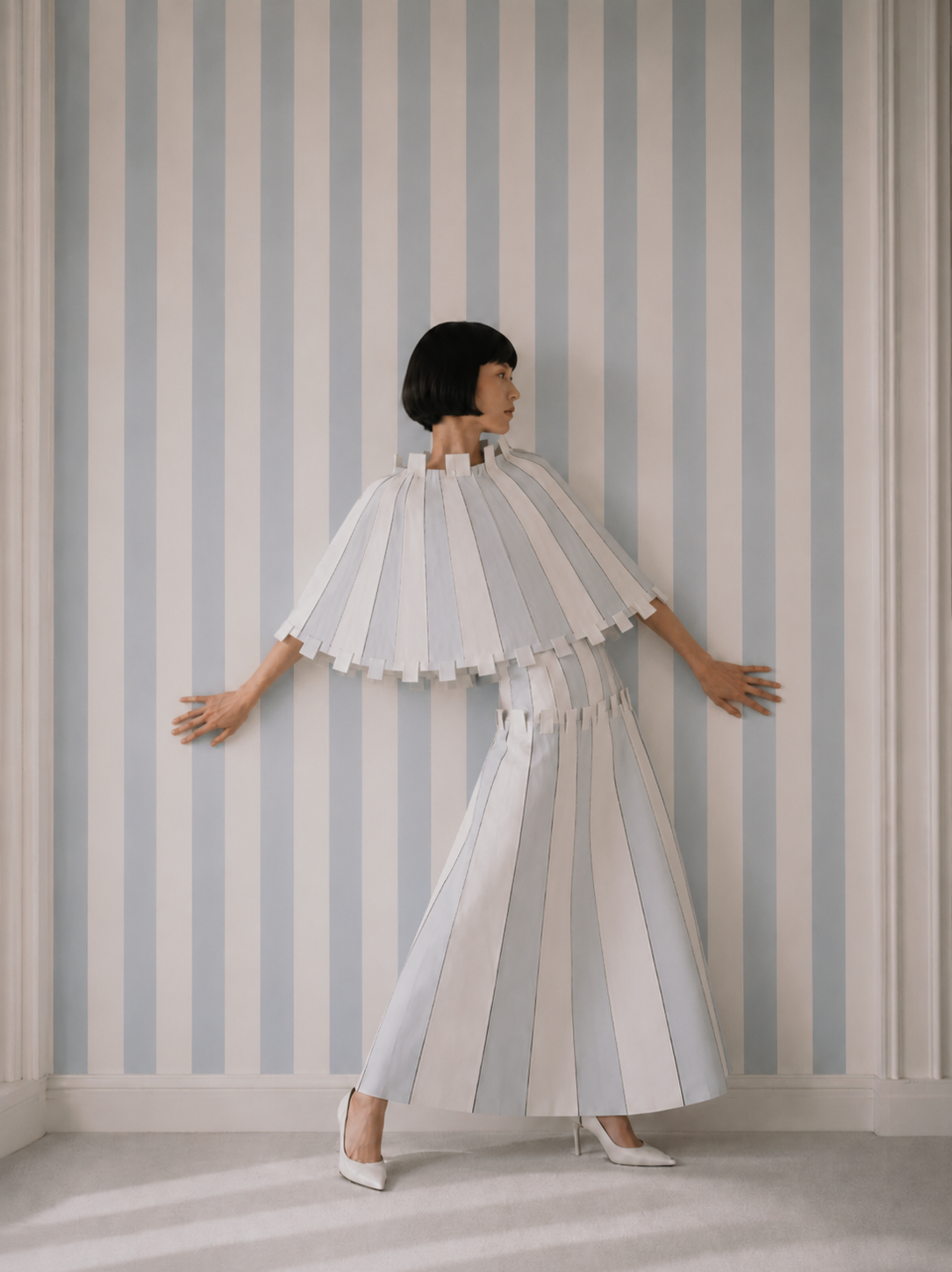 Femme de dos en ensemble origami bras écartés – papier peint rayé bleu et blanc