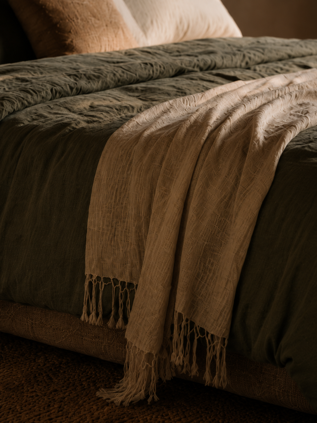 Plaid en lin naturel couleur caramel drapé en plis naturels sur une literie blanche