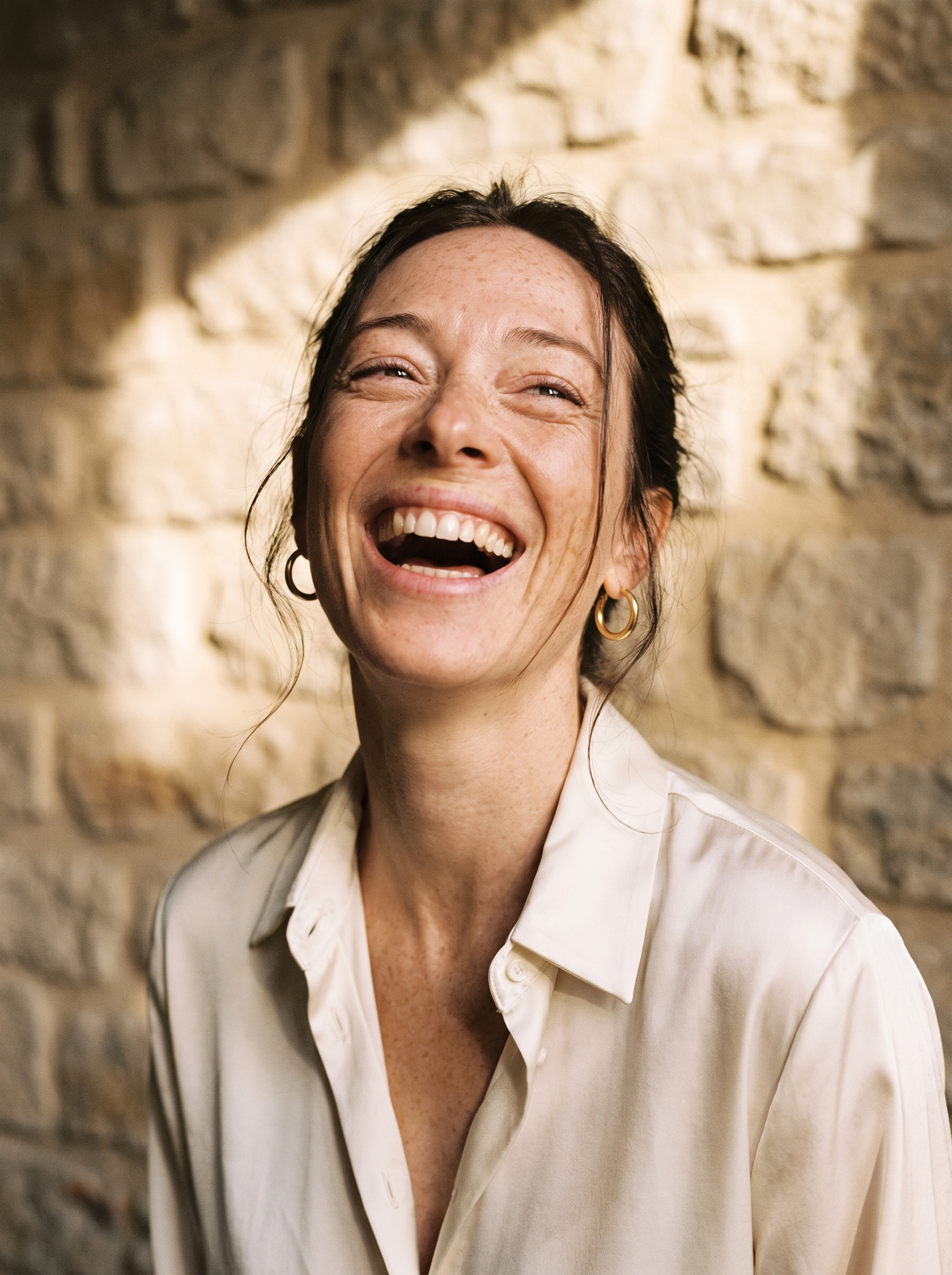 Portrait de femme brune riant aux éclats devant un mur en pierre