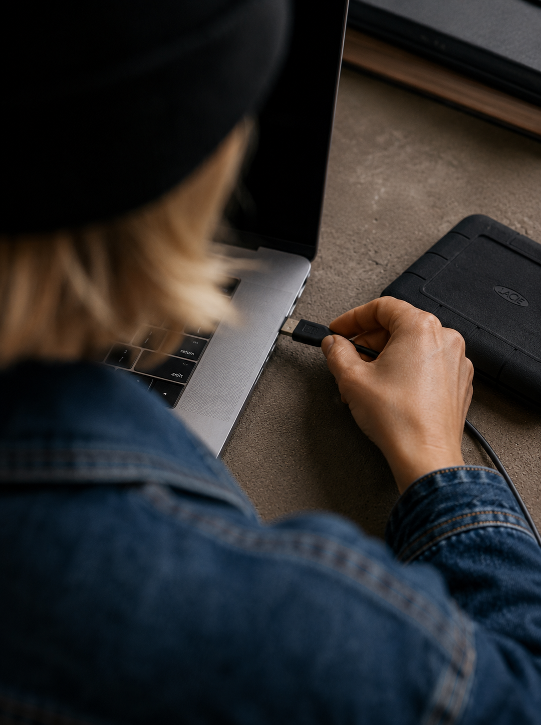 Main branchant une clé USB sur le port d'un laptop dans un bureau sombre avec disque dur externe à proximité
