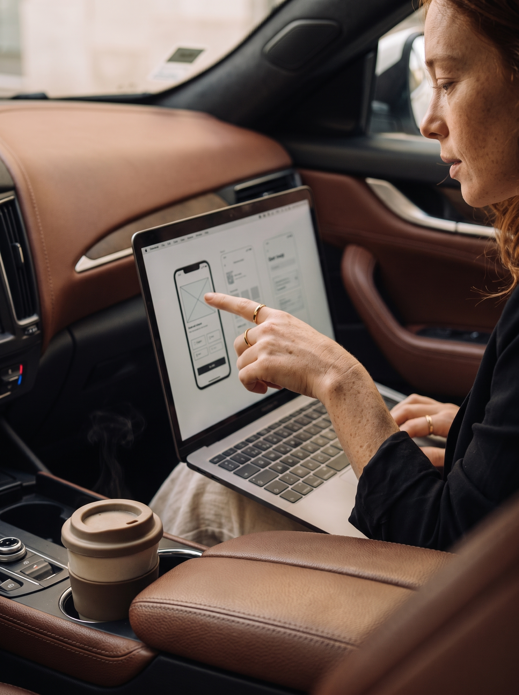 Femme rousse pointant des wireframes sur son laptop dans un véhicule de luxe
