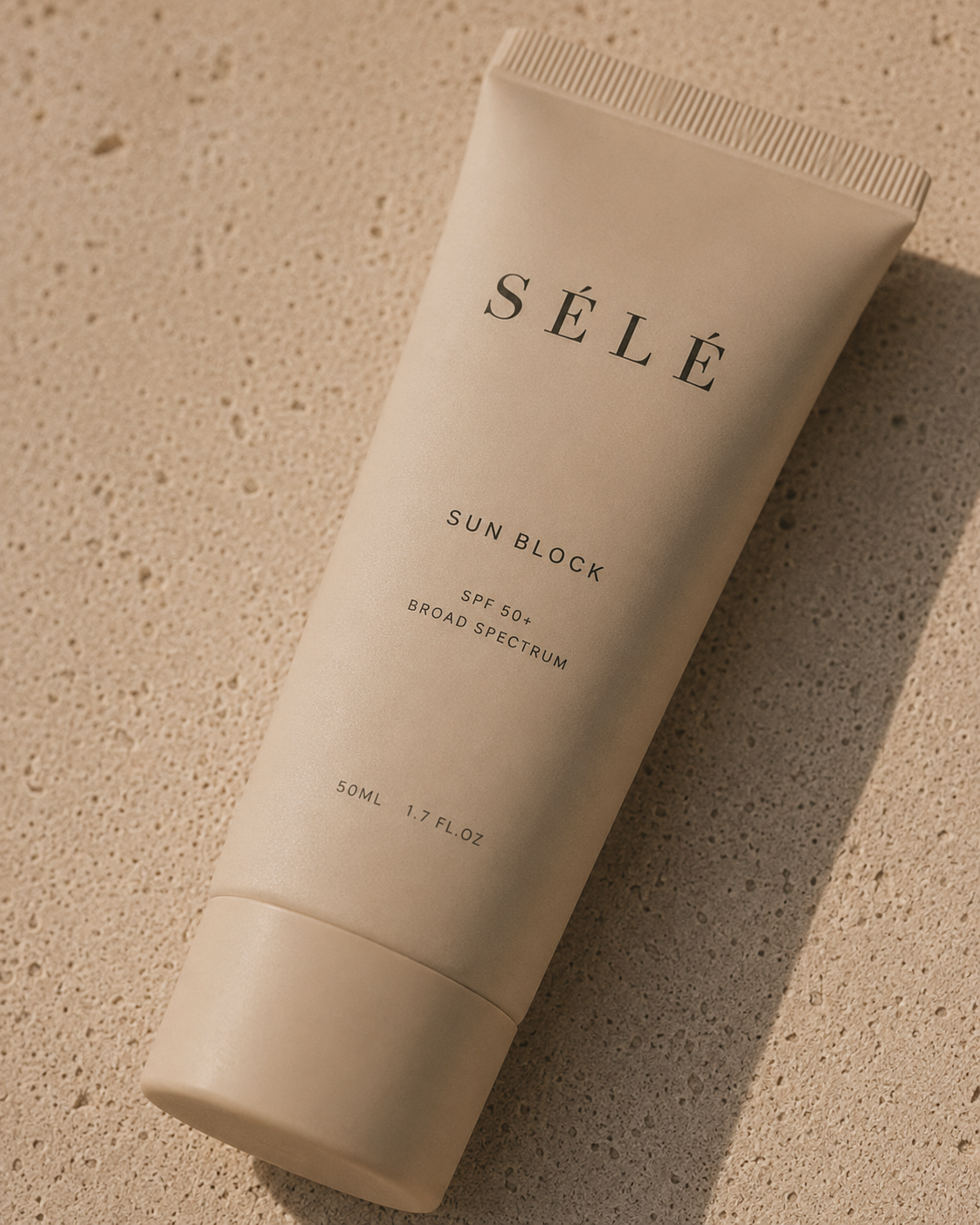 Tube crème solaire beige mat posé sur travertin texturé – lumière rasante, ombre portée, fond neutre