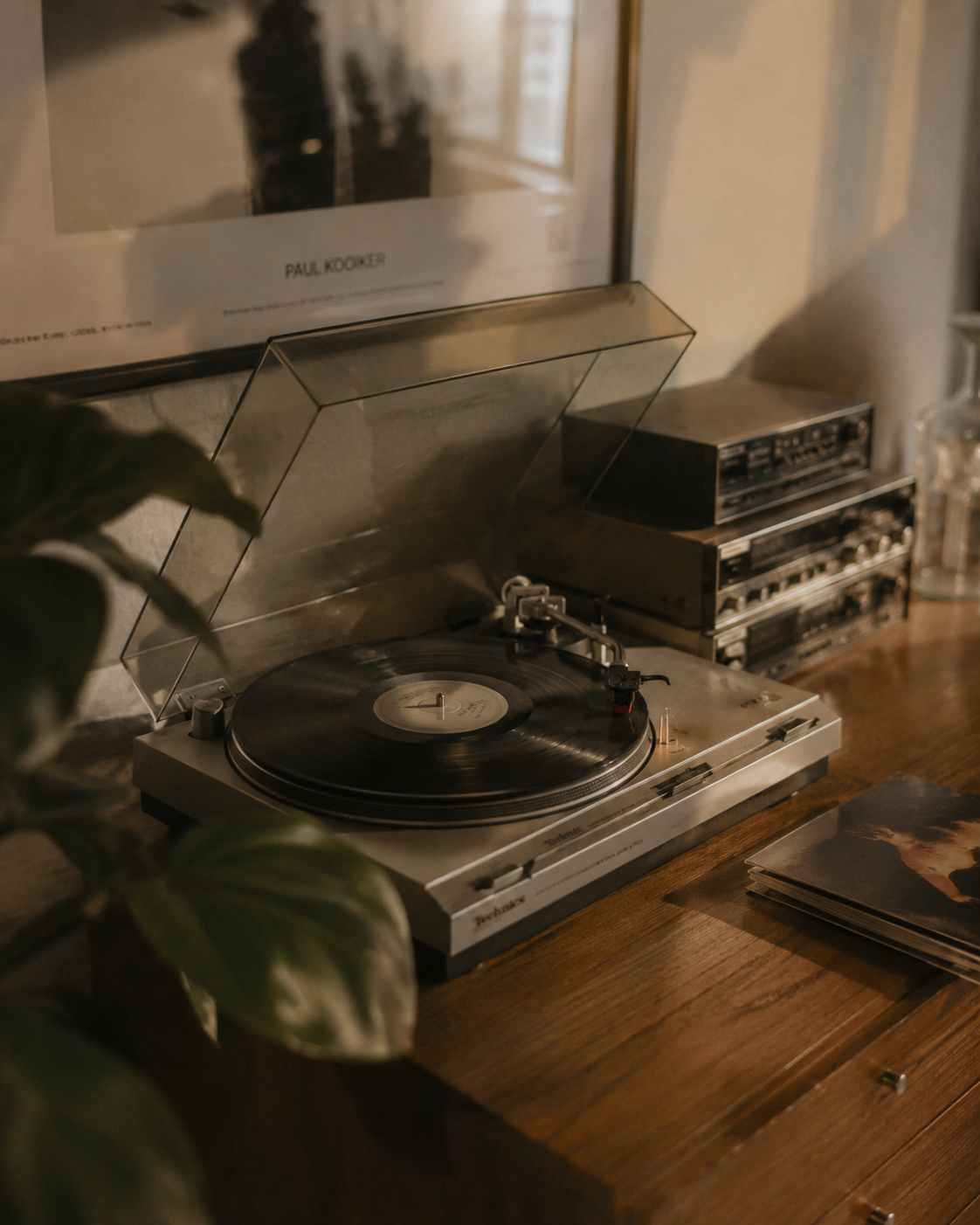 Platine vinyle sur meuble en bois – lumière chaude dorée, plante et ampli en fond