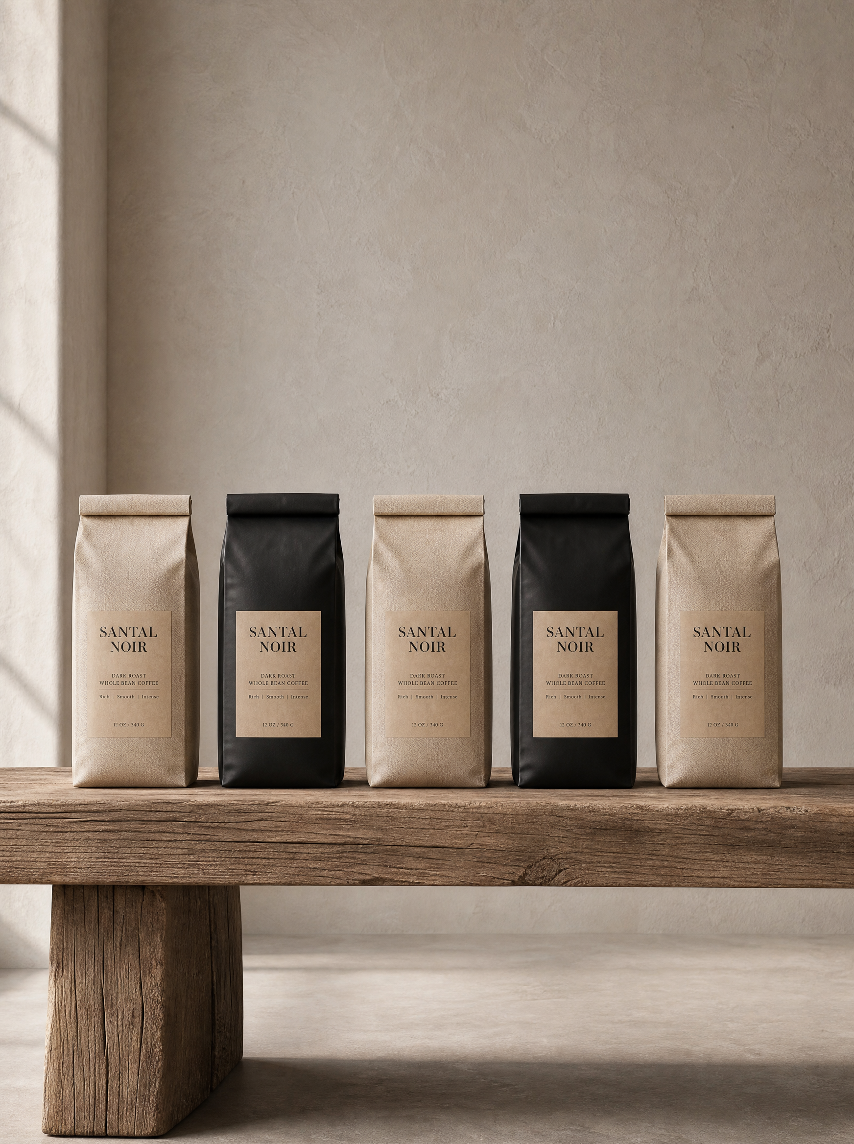 Cinq sachets café artisanal alignés – kraft et noir, banc bois rustique, mur beige, lumière latérale