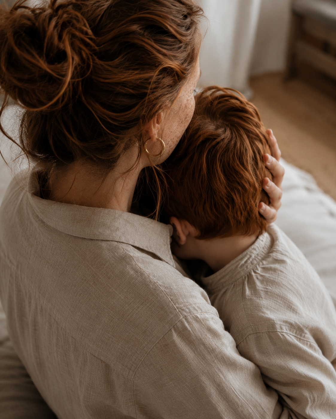 Femme de dos en chemise lin serrant un enfant roux – intérieur chaleureux et lumineux