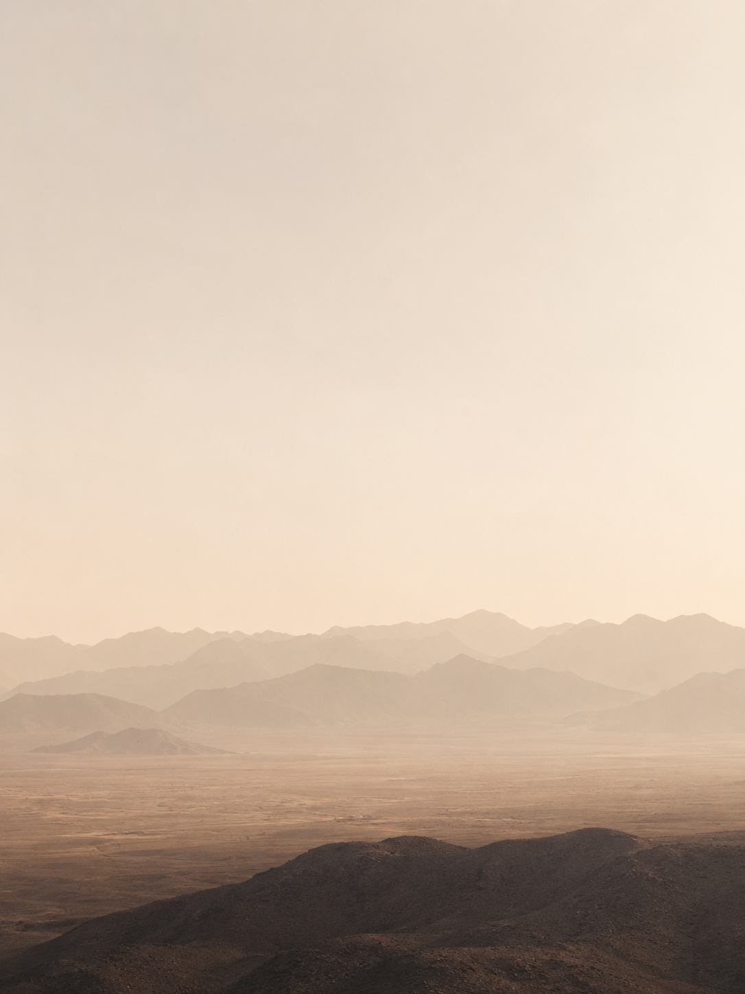Paysage désertique brumeux en couches – silhouettes de montagnes rosées, brume dorée, ciel pâle