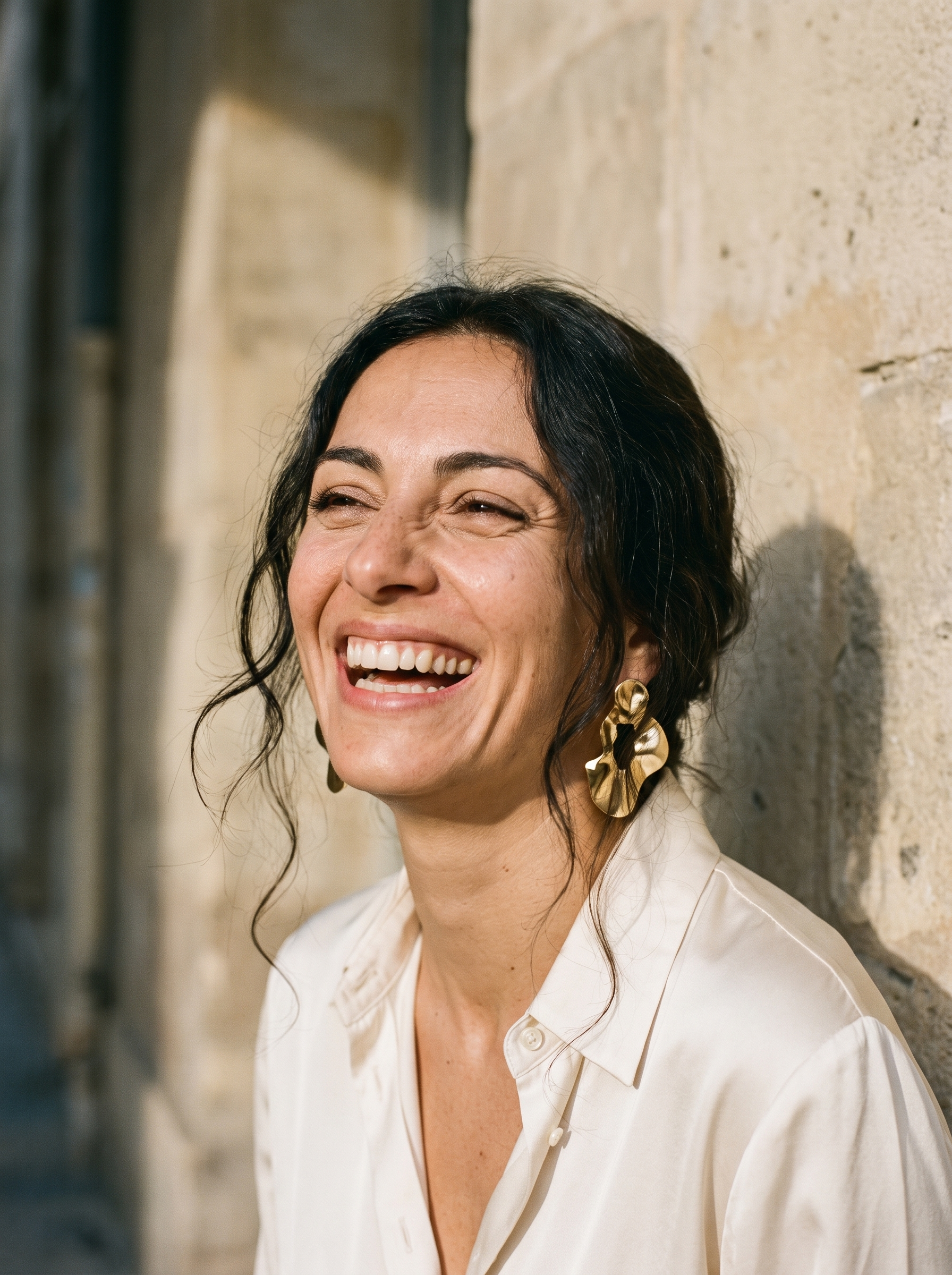 Portrait de femme brune riant aux éclats contre un mur en pierre