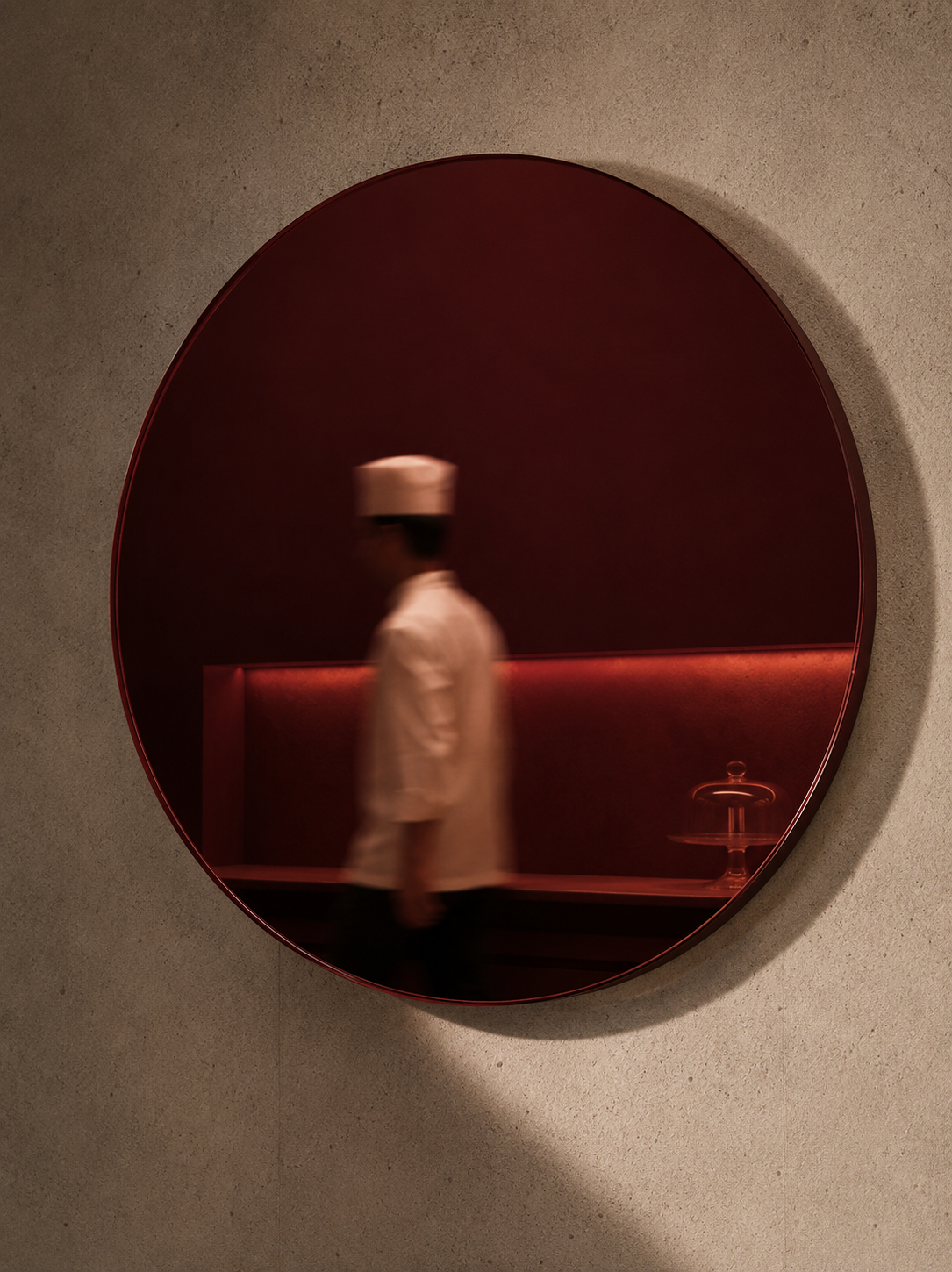 Miroir circulaire bordeaux sur mur beige – silhouette de cuisinier en toque, brasserie rouge en reflet