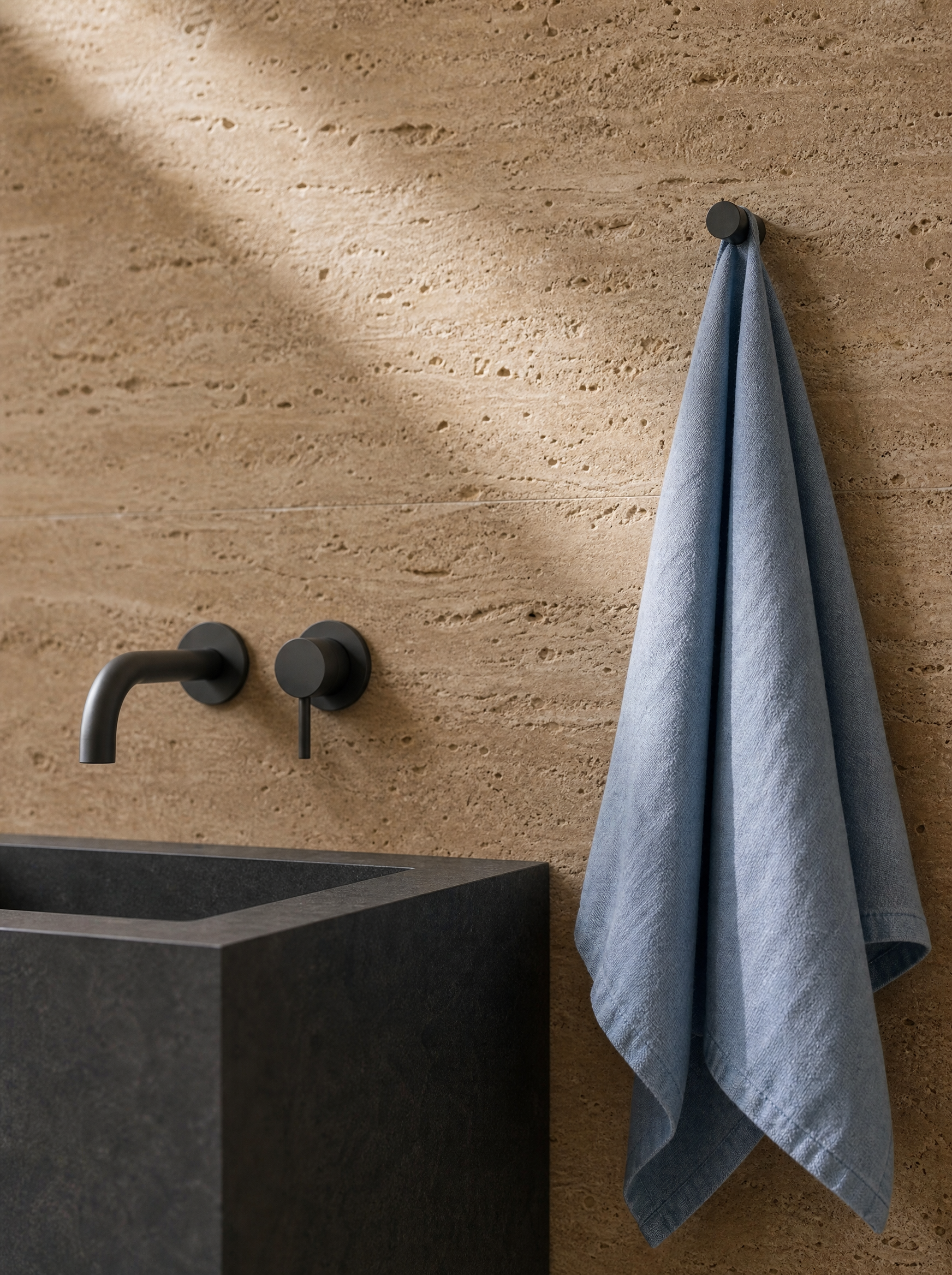 Salle de bain minimaliste avec vasque en béton, robinetterie encastrée et serviette en lin bleu sur travertin