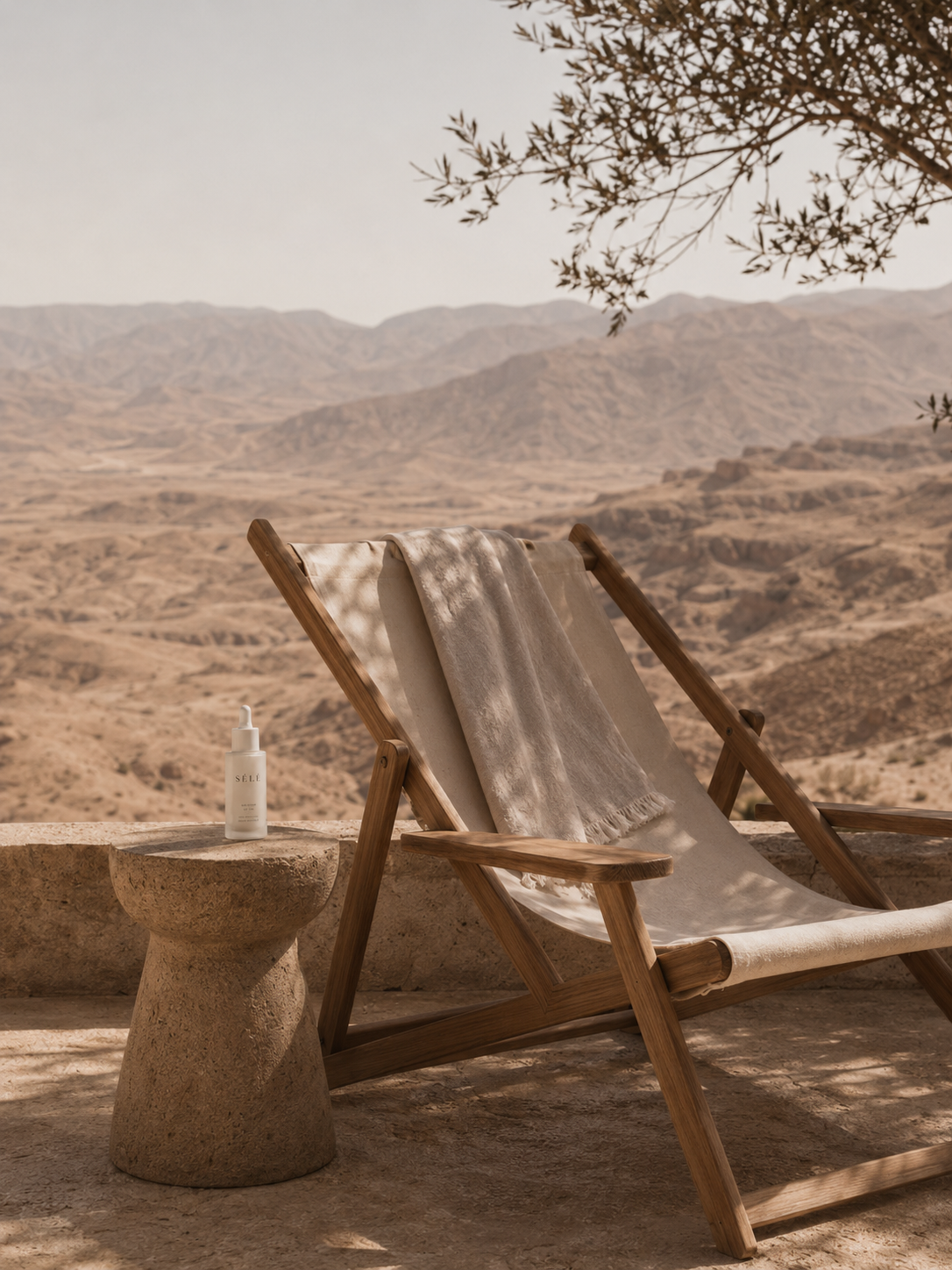 Chaise longue bois sur terrasse panoramique – table béton, flacon soin, vue désertique, olivier