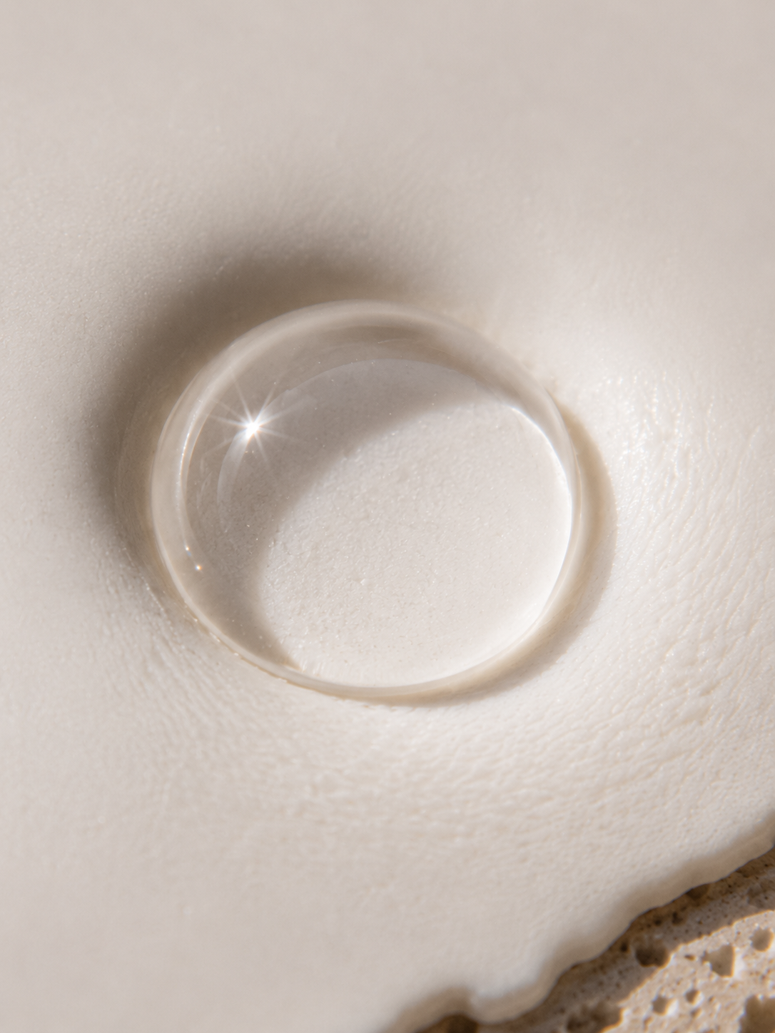 Macro goutte de sérum translucide avec reflet étoilé – crème blanche, fond plâtre, lumière douce