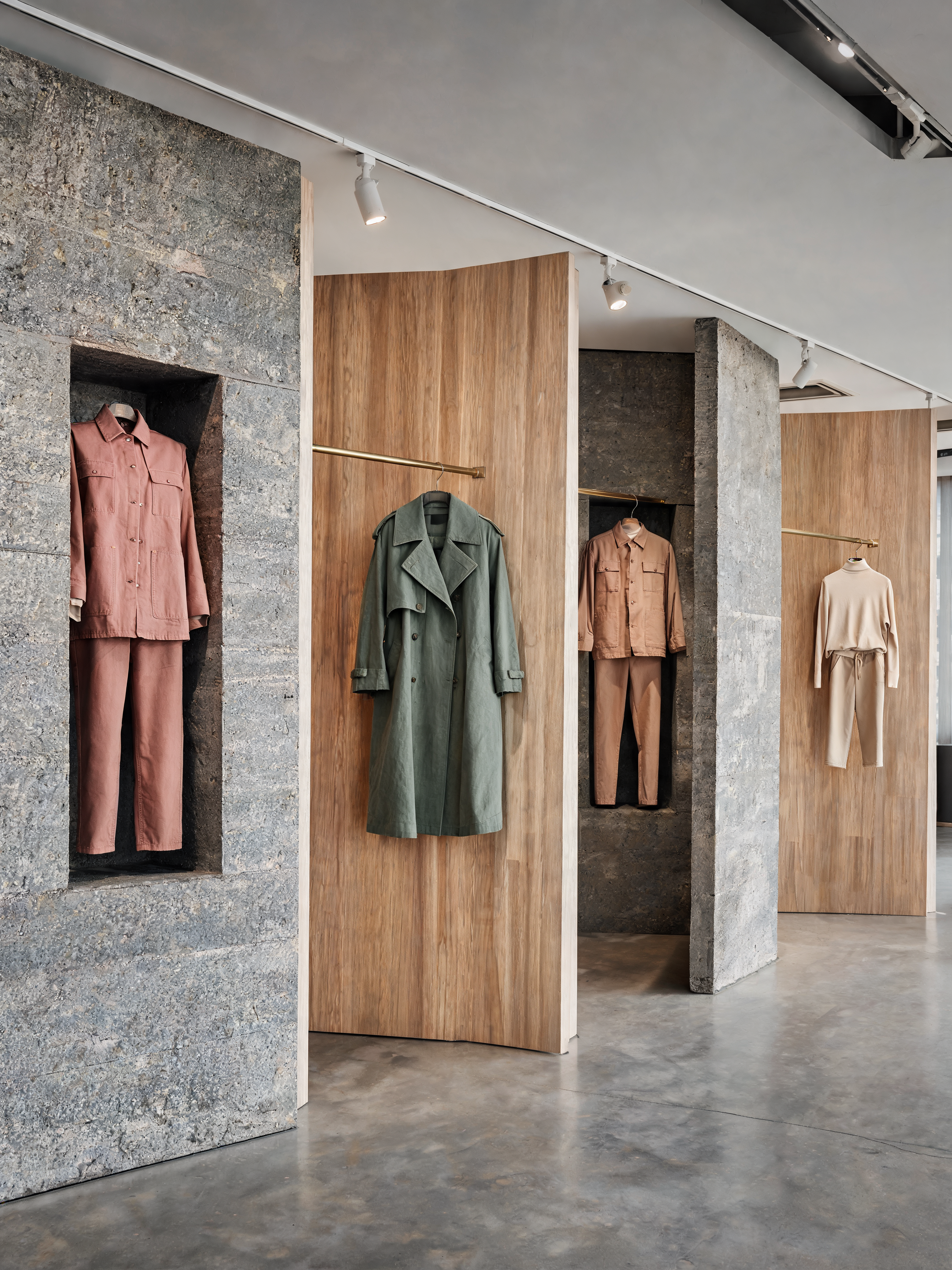 Boutique mode panneaux bois – niches béton, portants vêtements terracotta vert beige, couloir lumineux