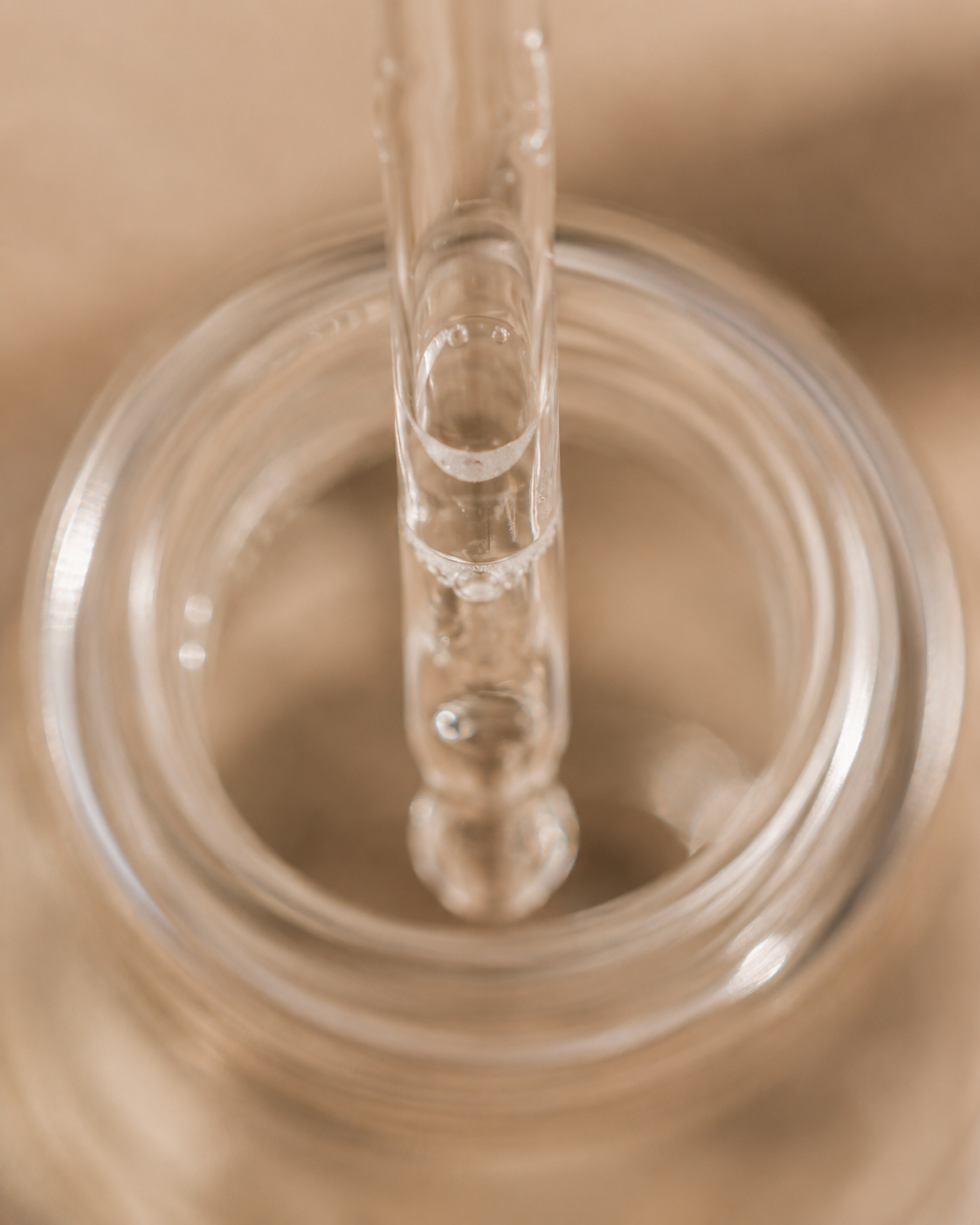 Macro pipette de verre plongeant dans flacon ouvert – bulles d'air, sérum translucide, fond beige
