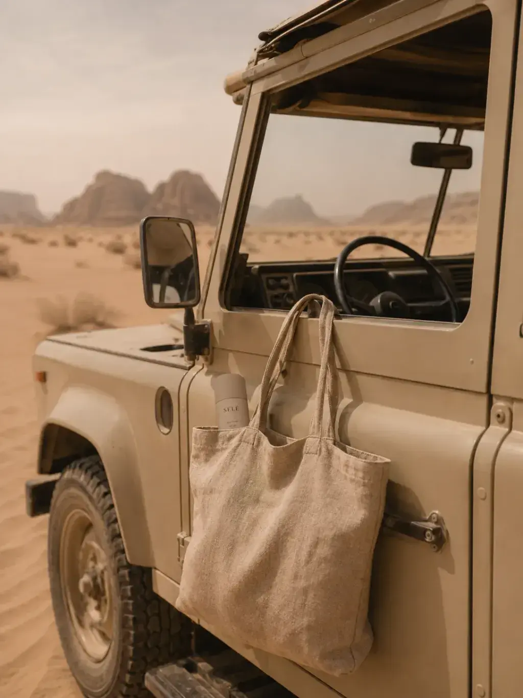 4x4 vintage beige dans le désert – tote bag lin à la portière, flacon soin, Wadi Rum, aventure