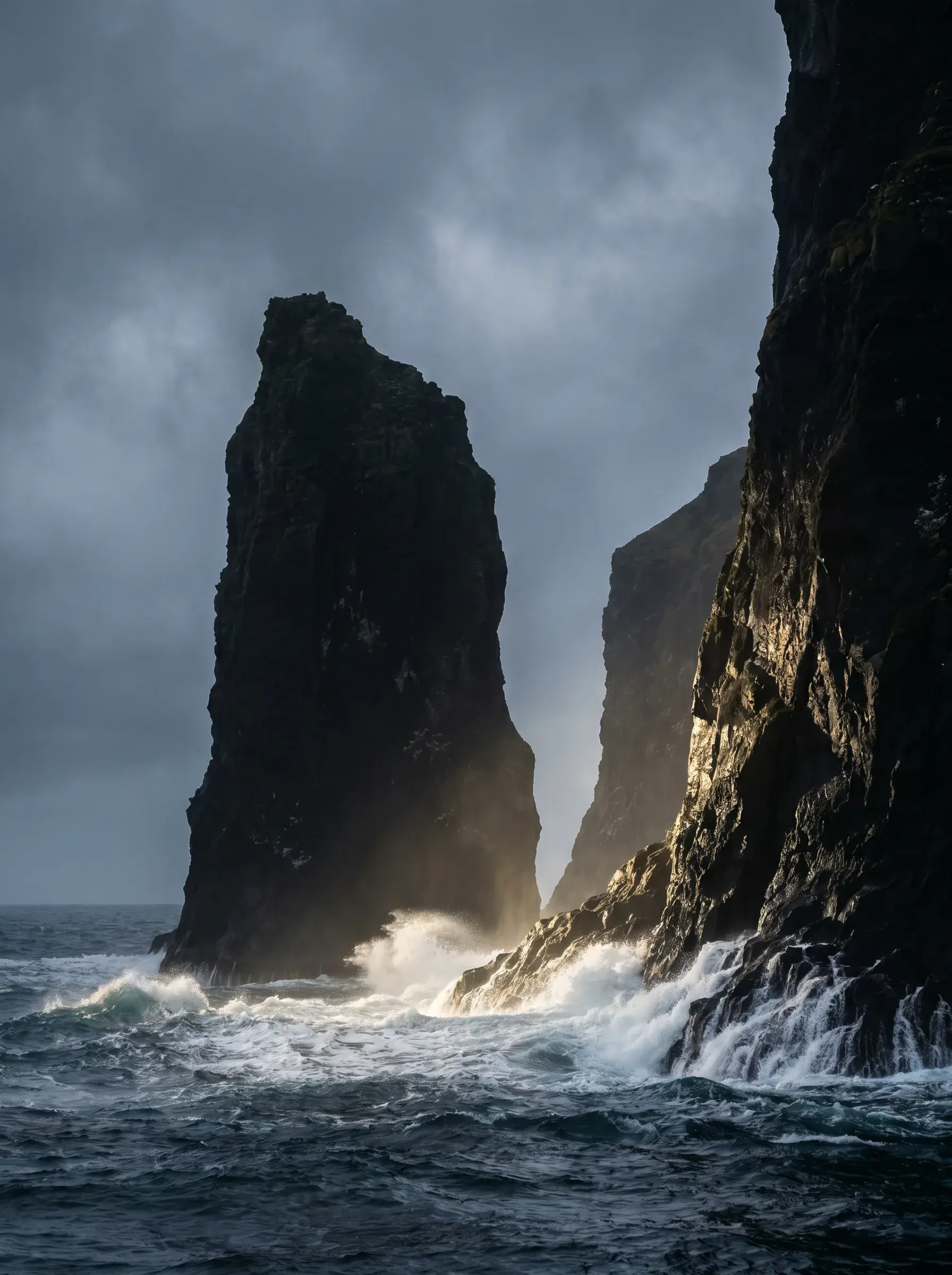 Aiguilles de basalte dans l'océan déchaîné – vagues écumantes, percée de lumière, ciel d'orage