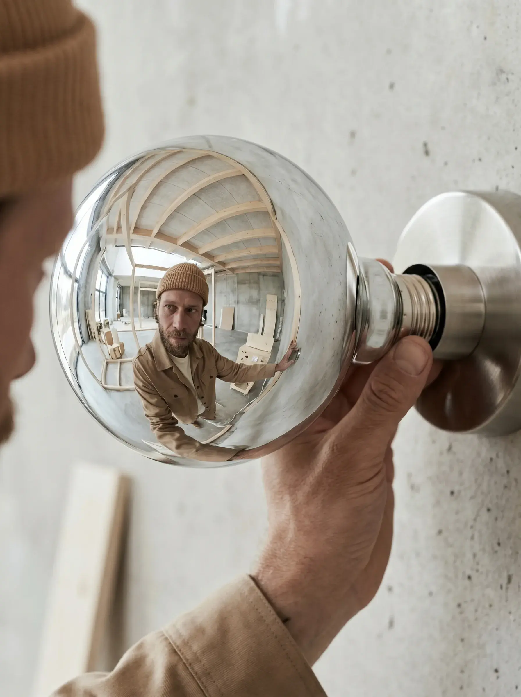 Ampoule globe chromée reflétant l'électricien et l'atelier, vissée sur un mur en béton
