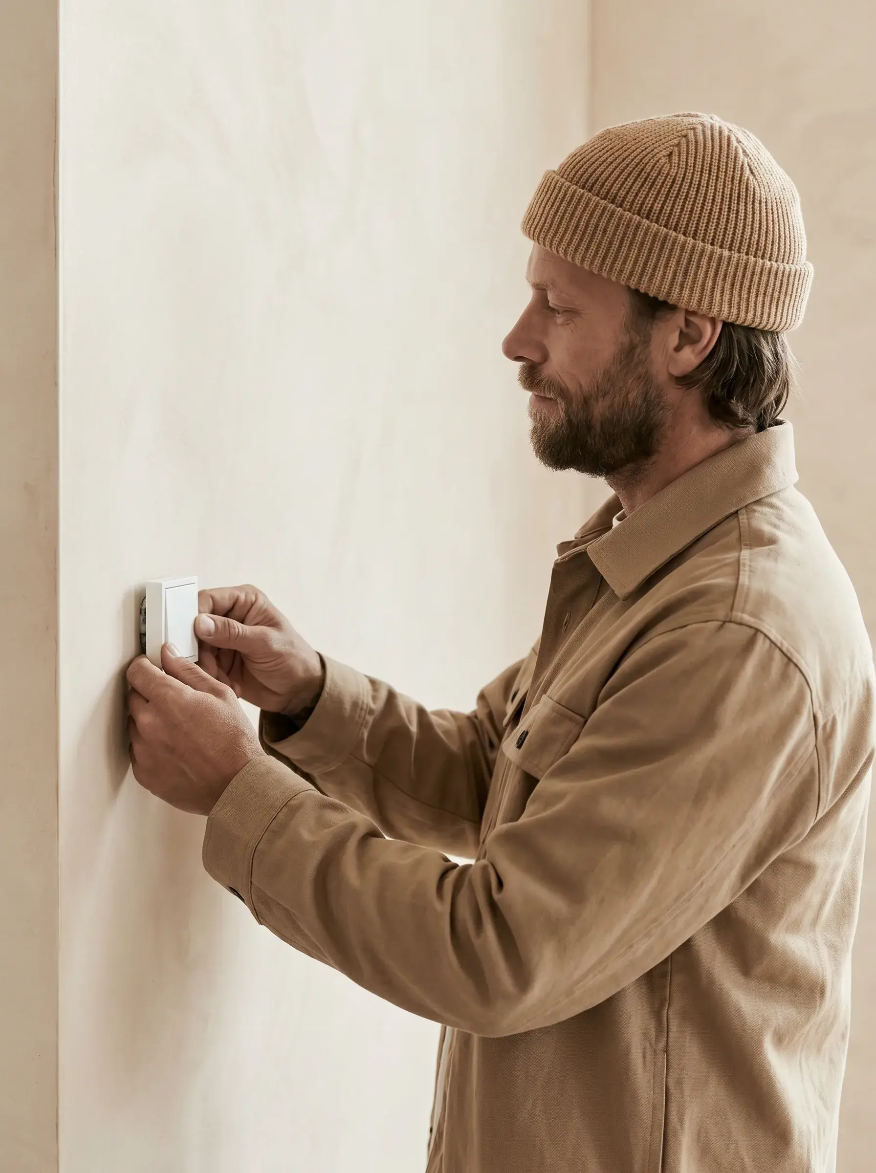 Artisan de profil fixant un boîtier blanc sur un mur en contreplaqué