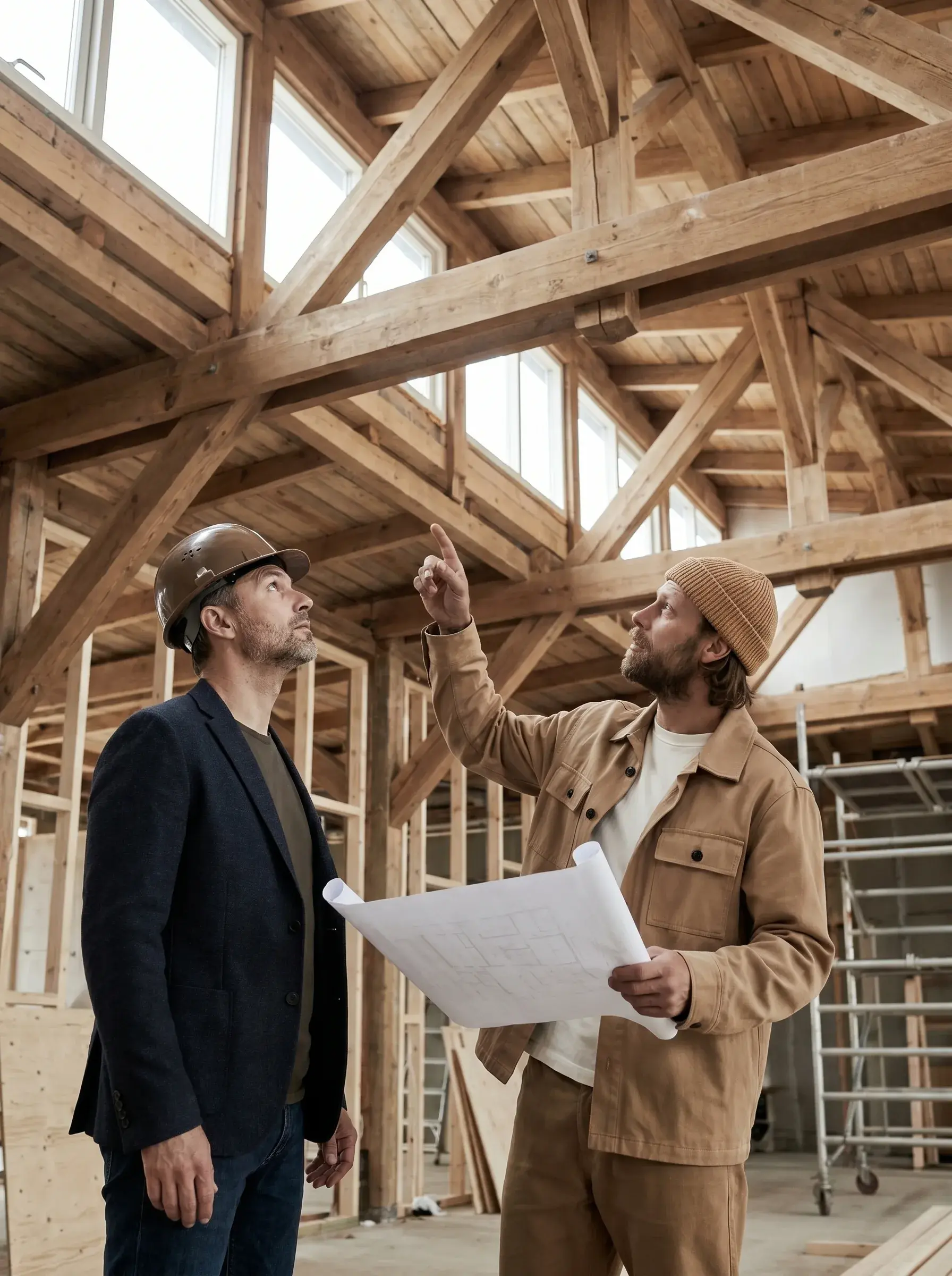 Artisan présentant les plans de la charpente à un maître d'ouvrage casqué sur le chantier