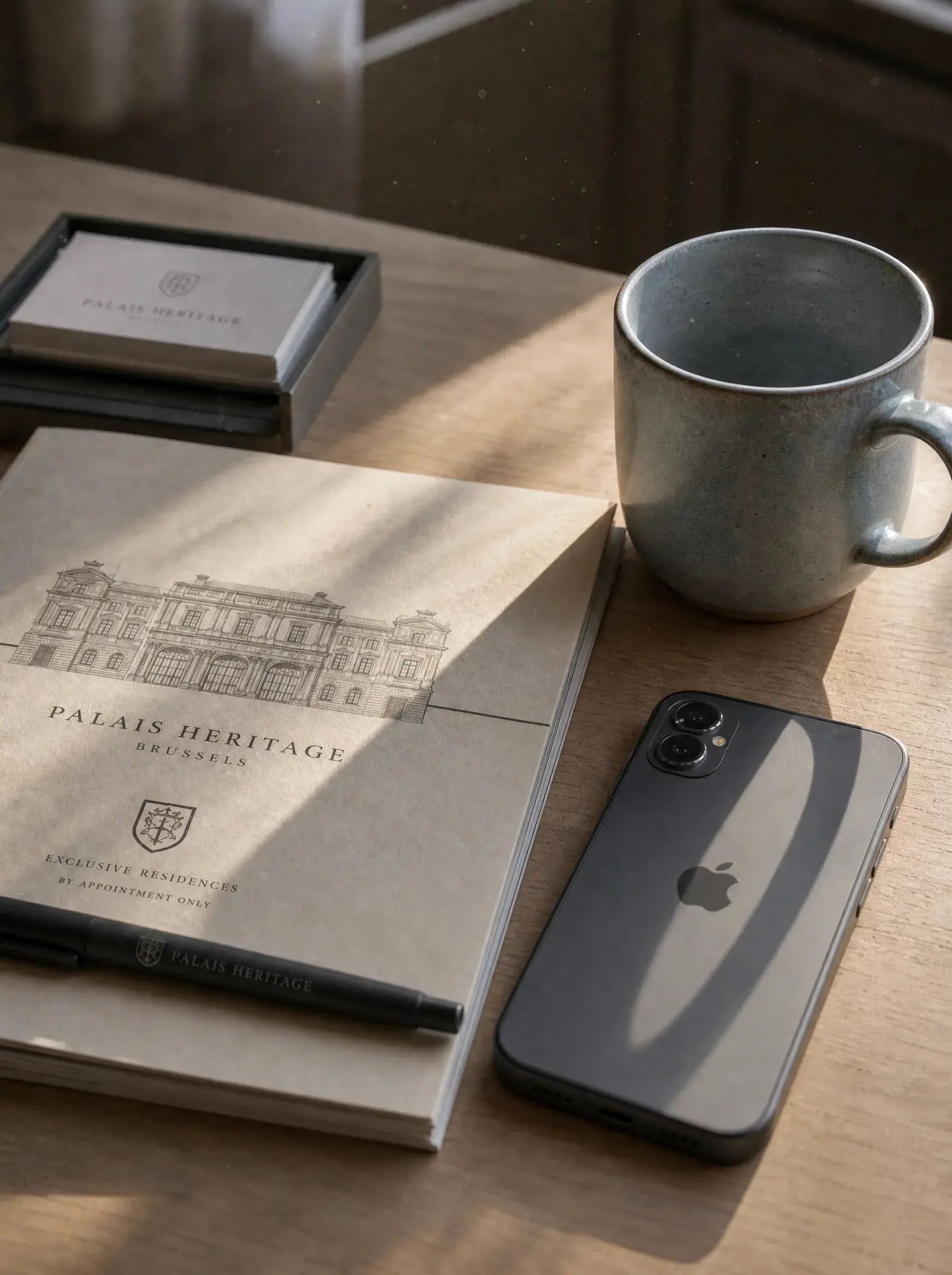 Brochure Palais Heritage Brussels, iPhone et mug en céramique sur table en bois à la lumière du matin