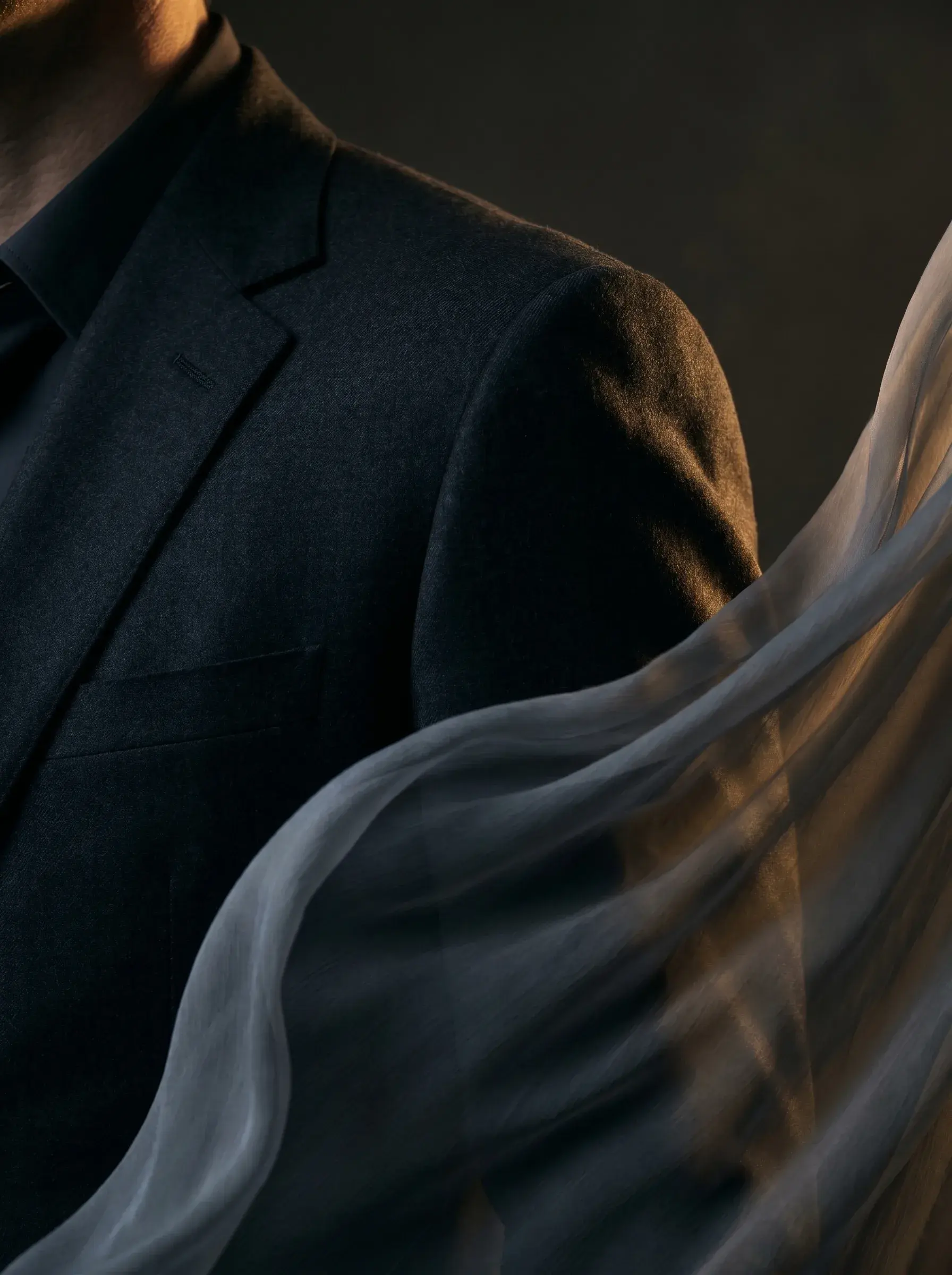 Buste homme en costume noir – voile gaze flottant en premier plan, lumière chaude directionnelle