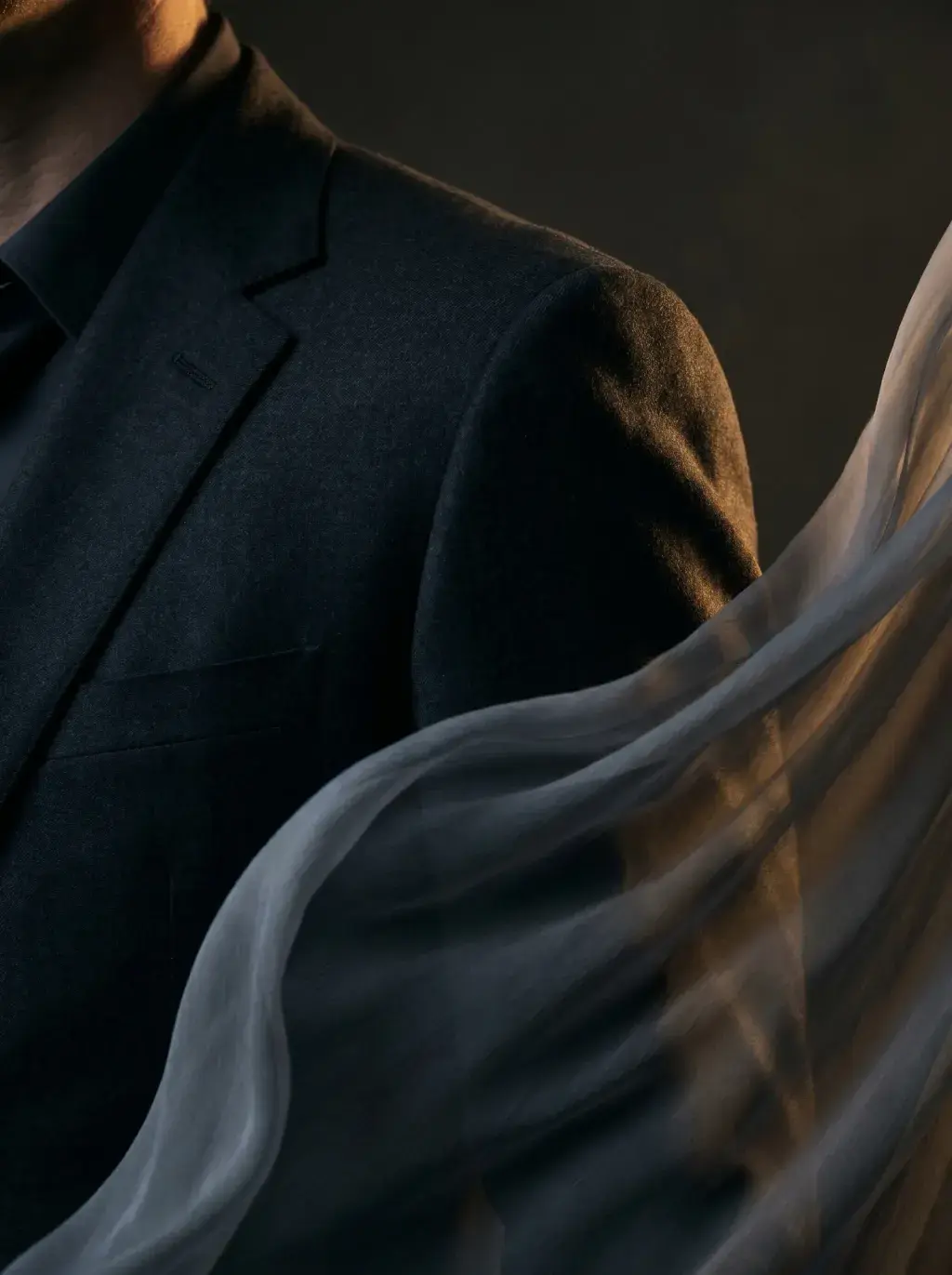 Buste homme en costume noir – voile gaze flottant en premier plan, lumière chaude directionnelle