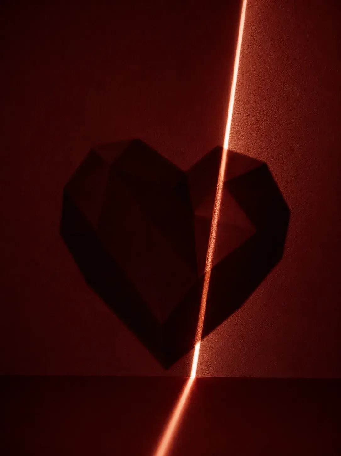 Cœur géométrique facetté sombre avec rayon de lumière néon orange traversant le fond rouge bordeaux profond