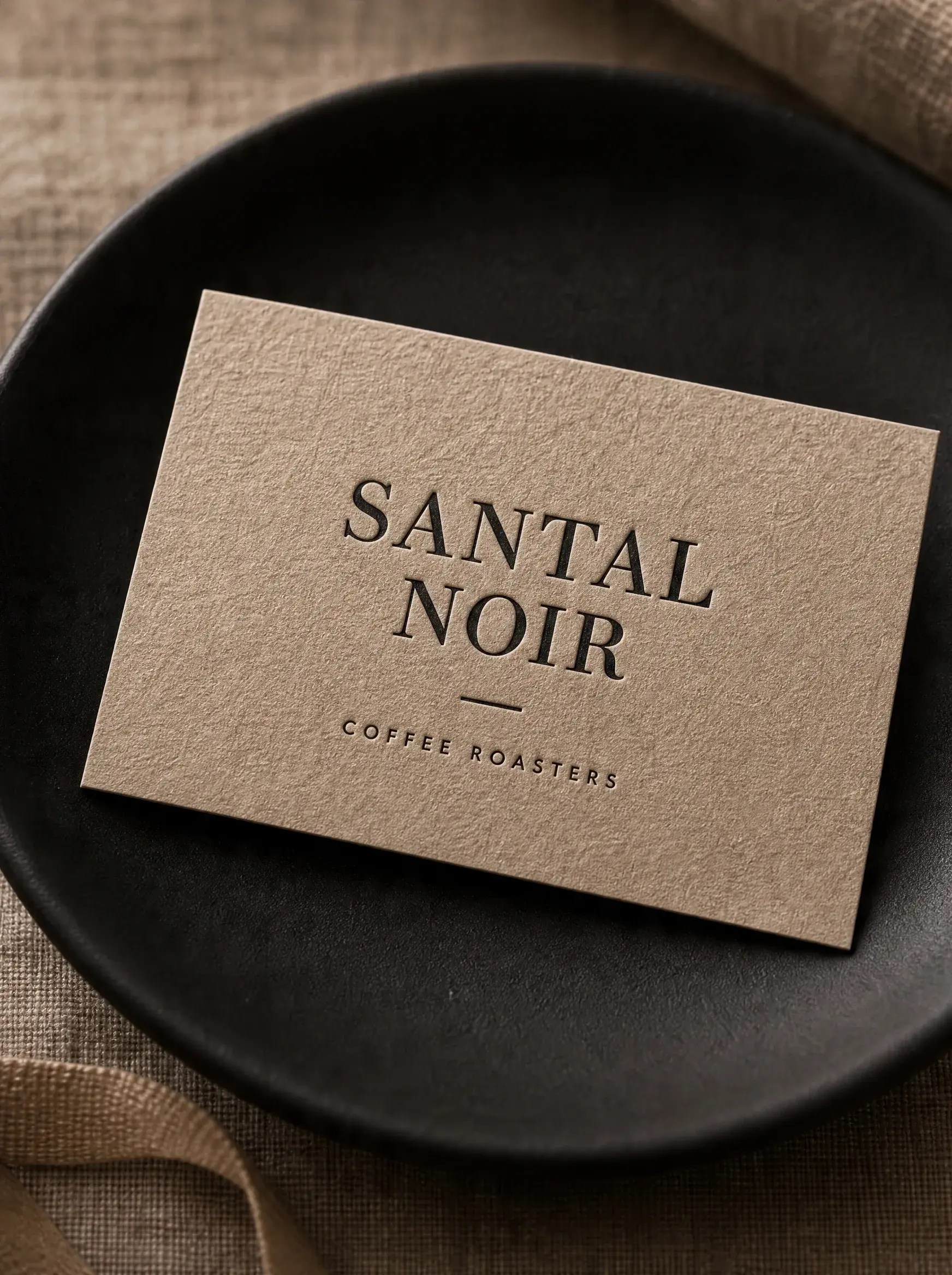 Carte de visite kraft avec typographie gaufrage sur assiette céramique noire – nappe lin