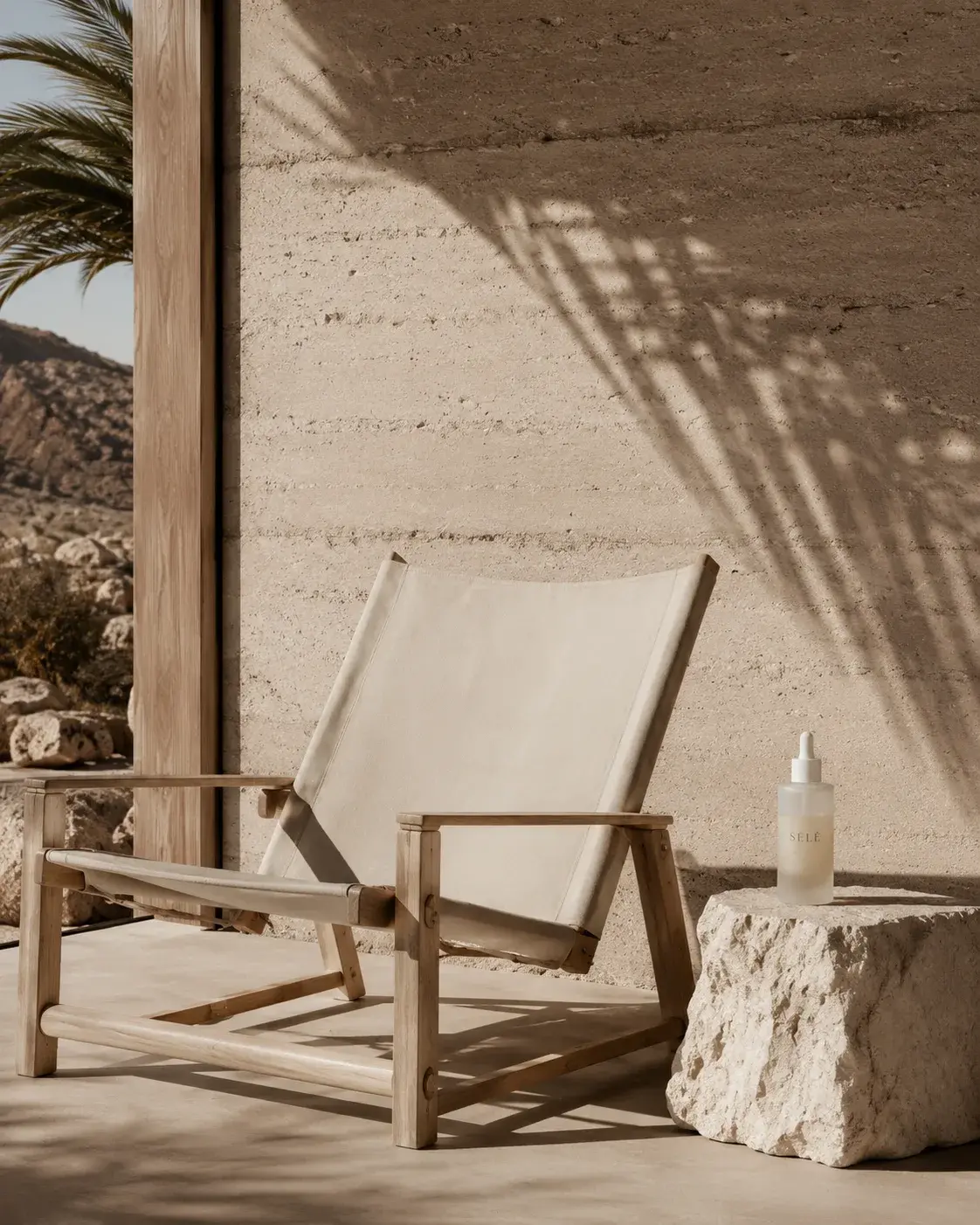 Chaise longue bois et toile blanche sur terrasse désertique – ombre de palmier, flacon soin, rocher