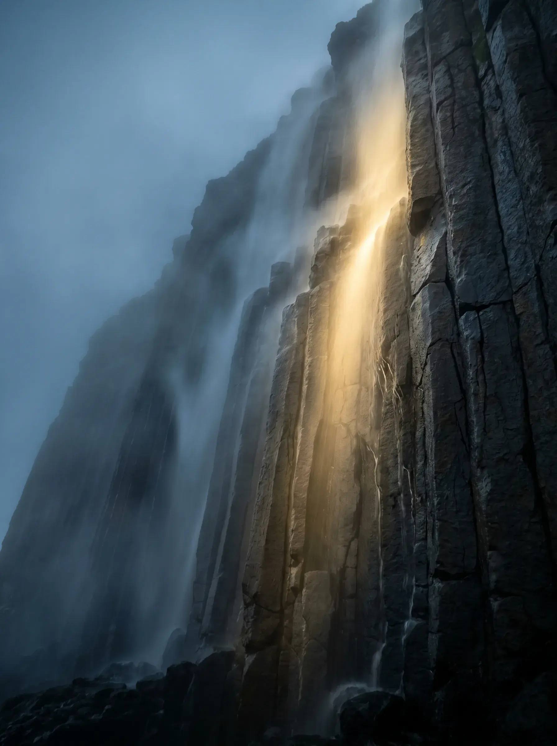 Chute d'eau sur falaise de basalte hexagonal – rayon de lumière doré, brume, vue vers le haut