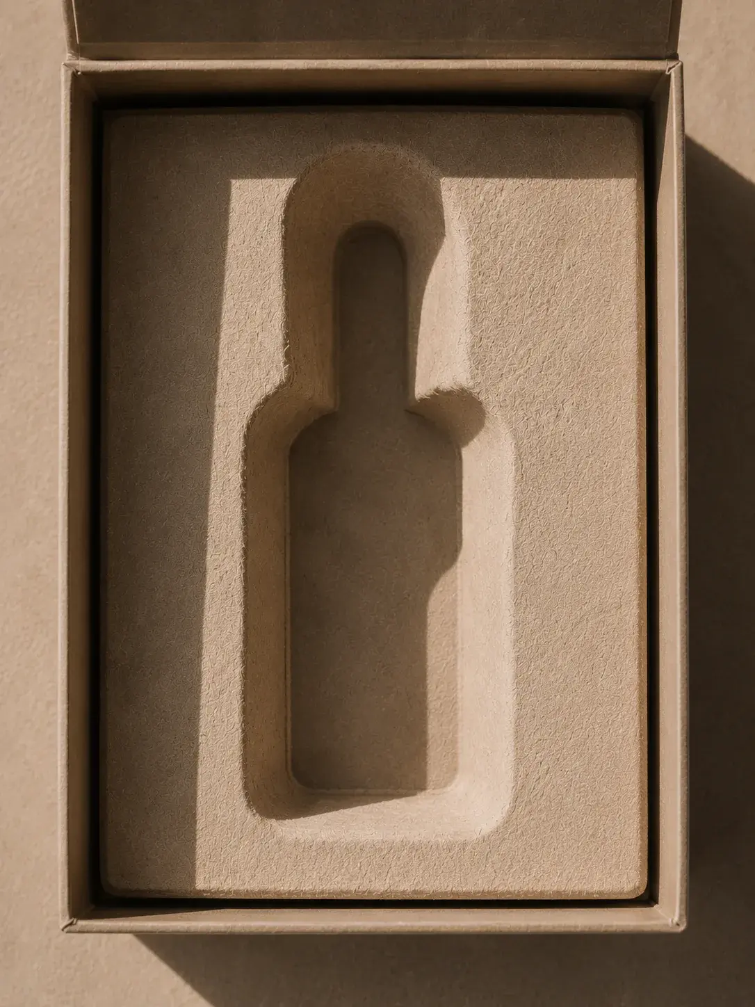 Coffret kraft vide ouvert – empreinte mousse en forme de flacon, ombres graphiques, vue de dessus