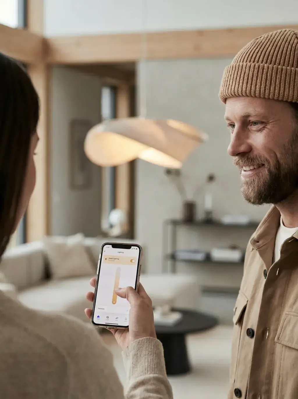 Couple réglant l'éclairage connecté sur smartphone sous une suspension design en bois