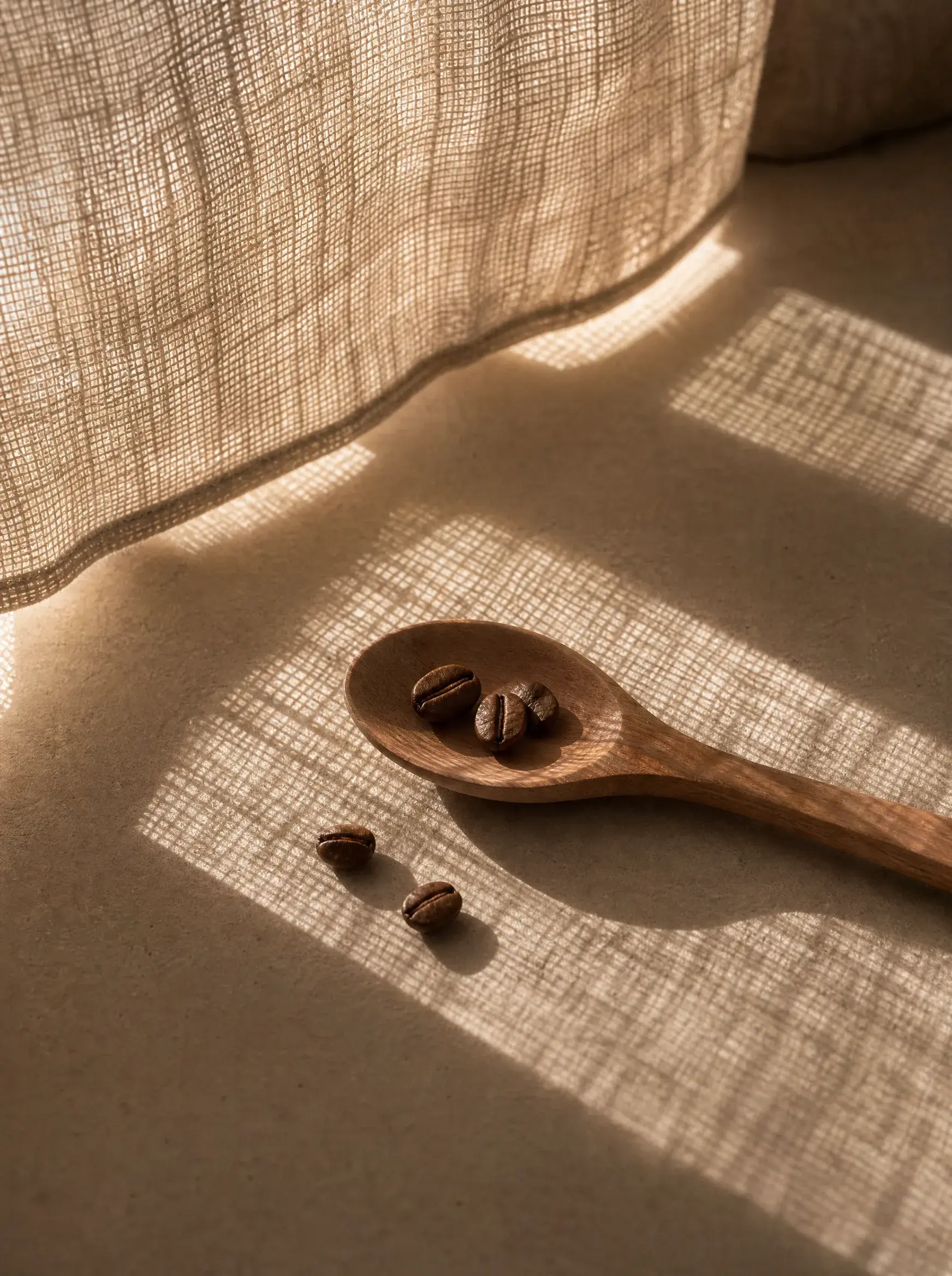 Cuillère bois avec trois grains de café – fond beige, rideau lin, lumière quadrillée