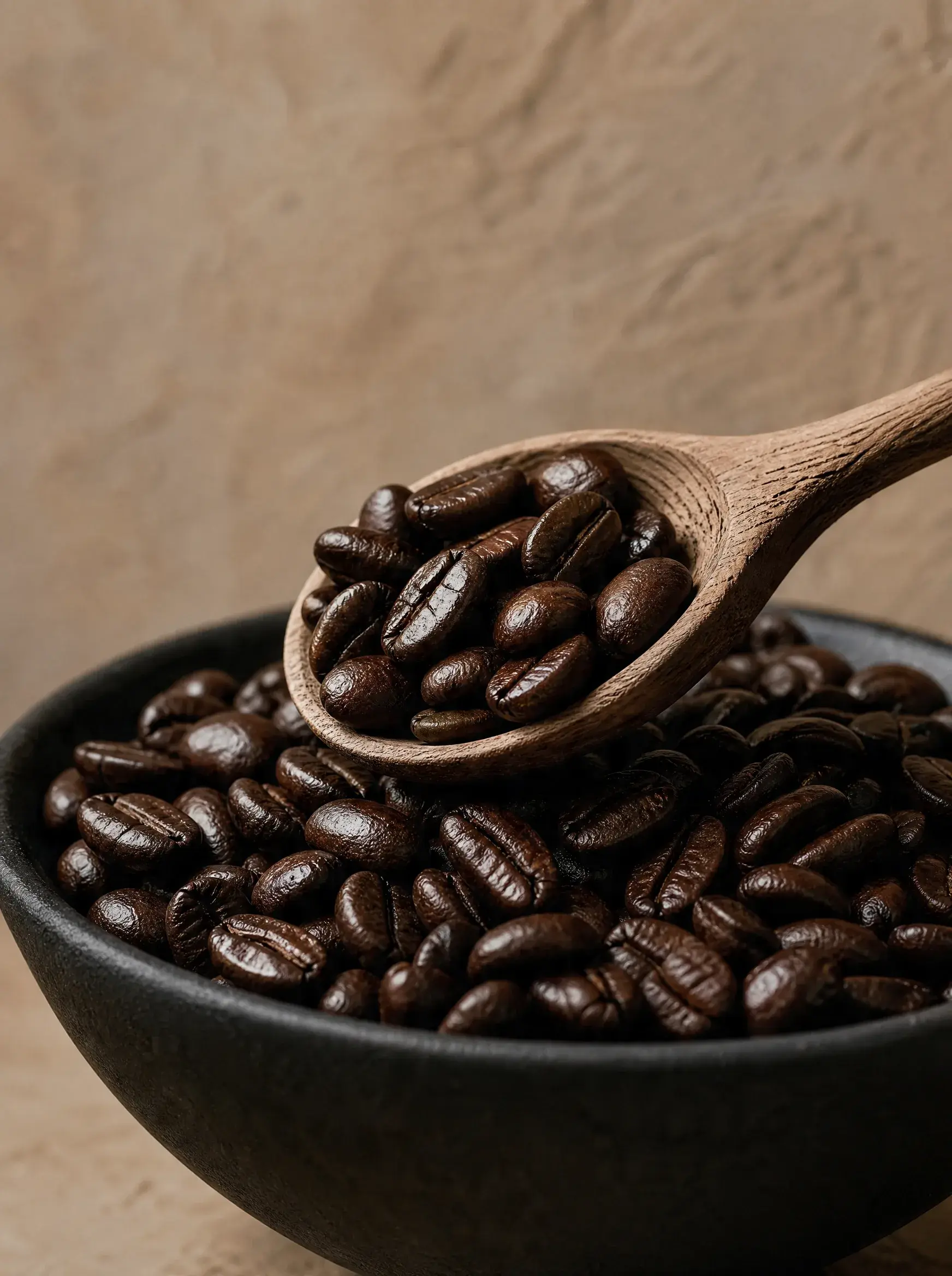 Cuillère bois pleine grains café au-dessus bol céramique noire – fond beige texturé, gros plan