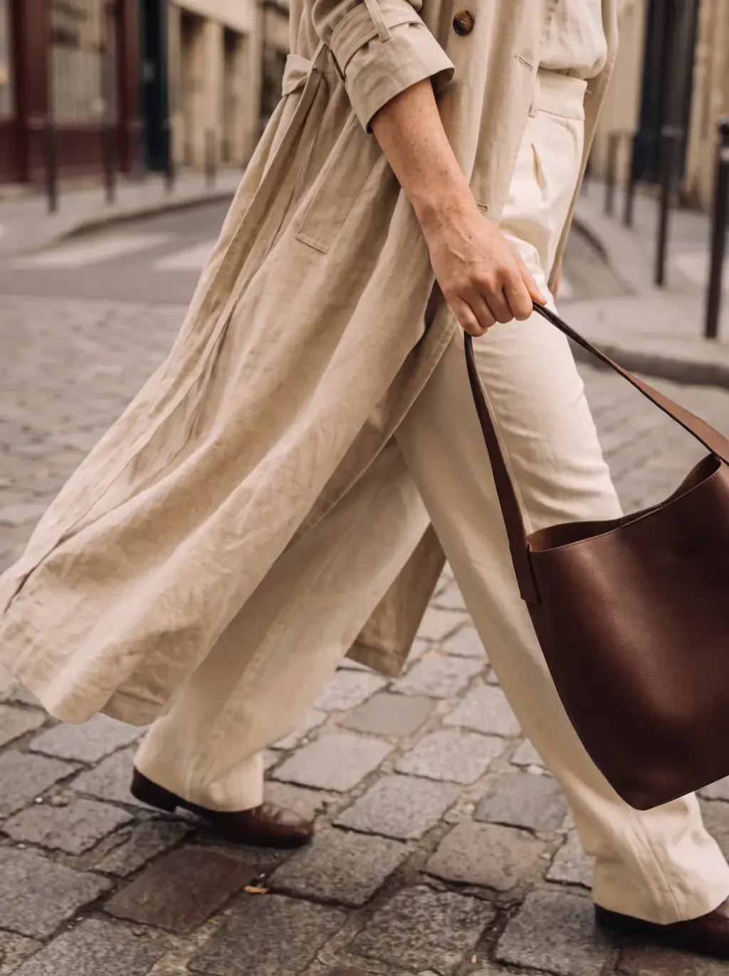 Détail mode d'une femme marchant sur les pavés parisiens avec sac cabas brun et trench lin