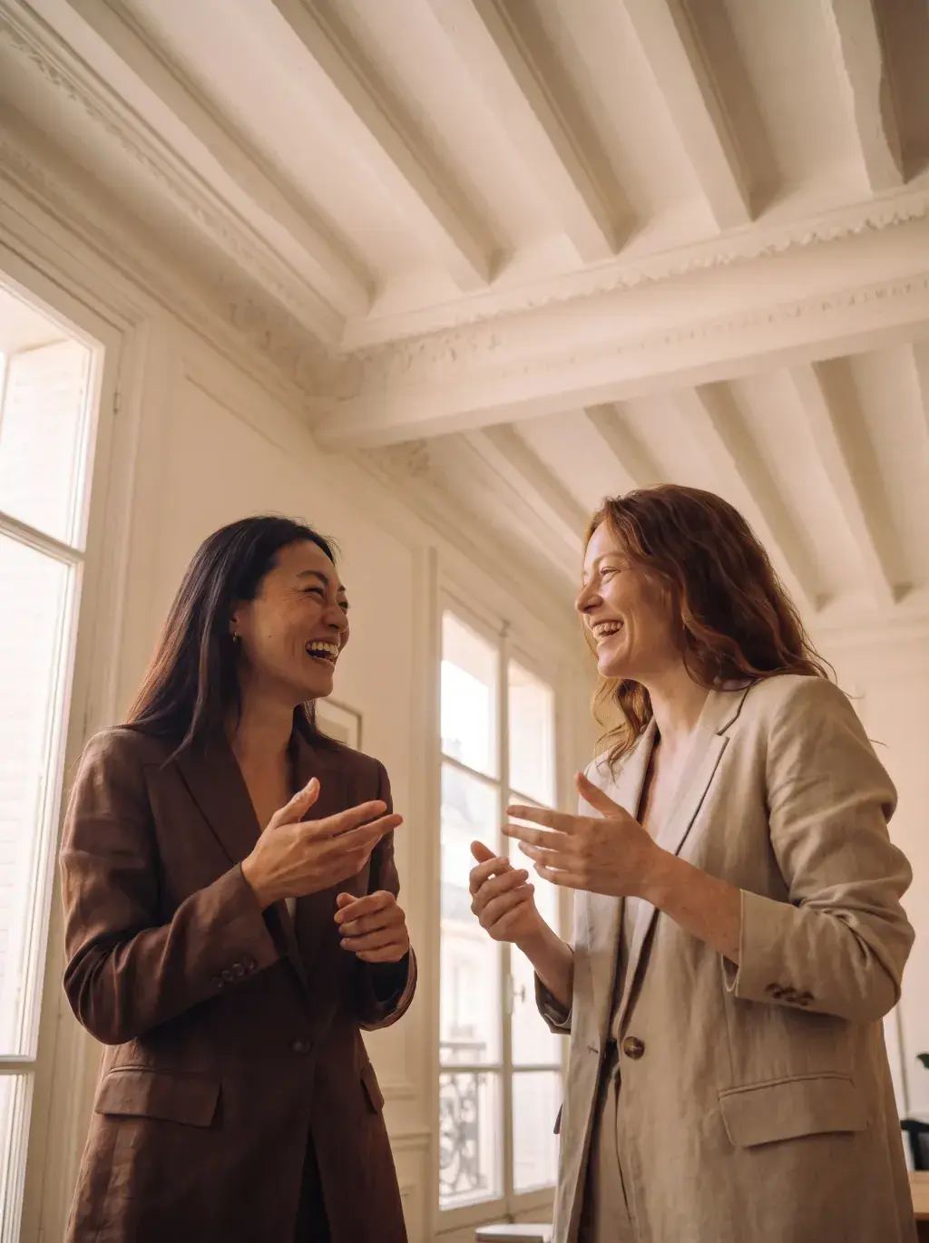 Deux associées en conversation joyeuse dans un appartement parisien lumineux aux moulures