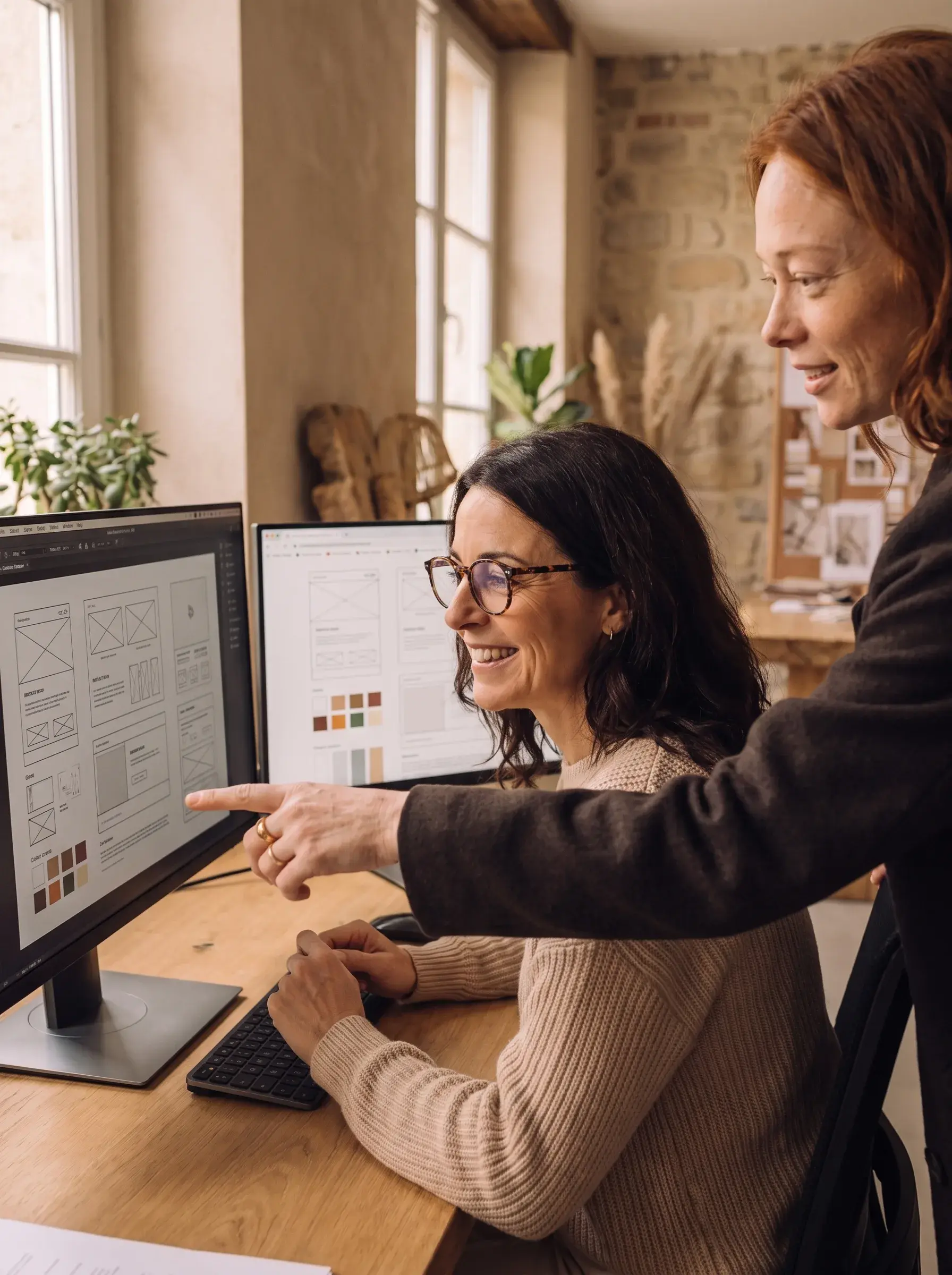Deux designers pointant des wireframes UI sur un grand écran dans un studio avec panneau de liège