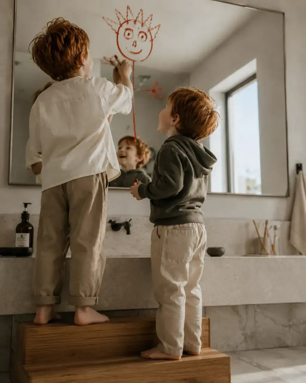 Deux garçons roux dessinant un soleil sur le miroir de la salle de bain