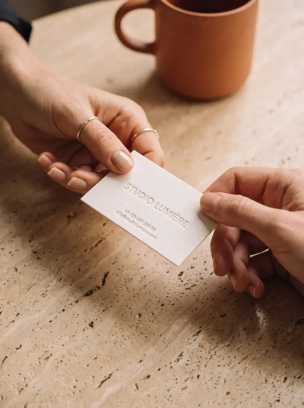 Deux mains échangeant une carte de visite Studio Lumière sur une table en marbre