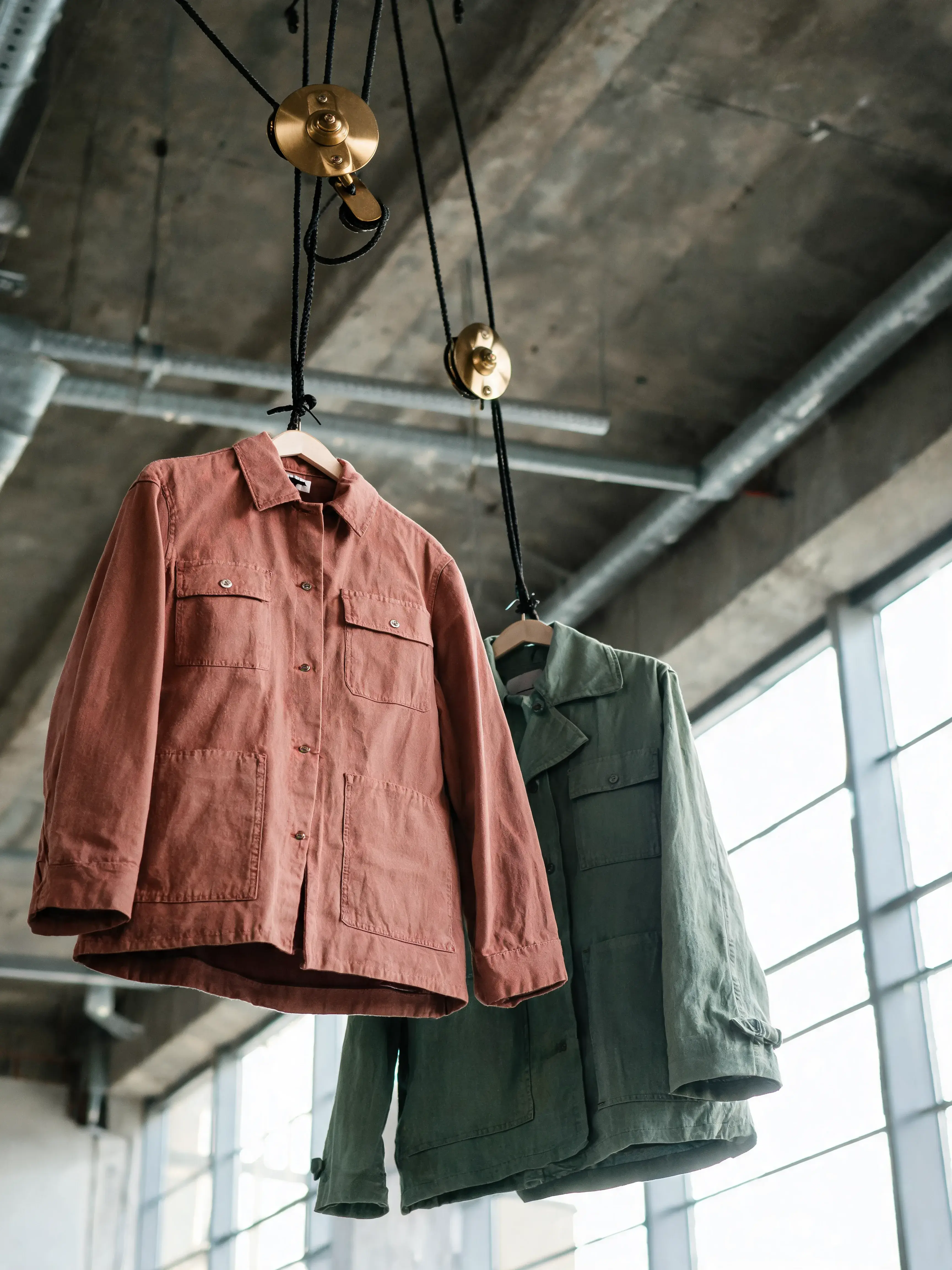 Deux vestes suspendues câbles laiton poulies – terracotta et kaki, fenêtre atelier industriel
