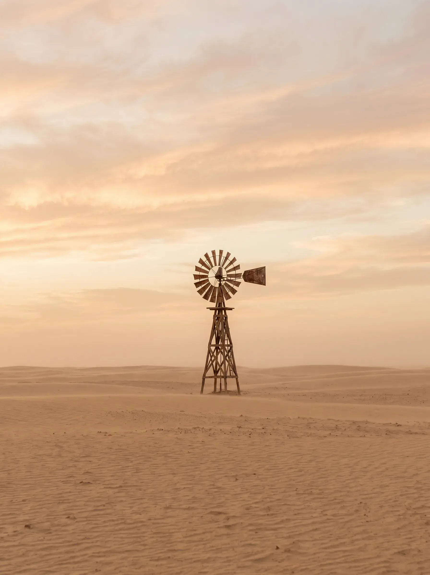 Éolienne ancienne solitaire dans un désert de sable doré au coucher de soleil nuageux