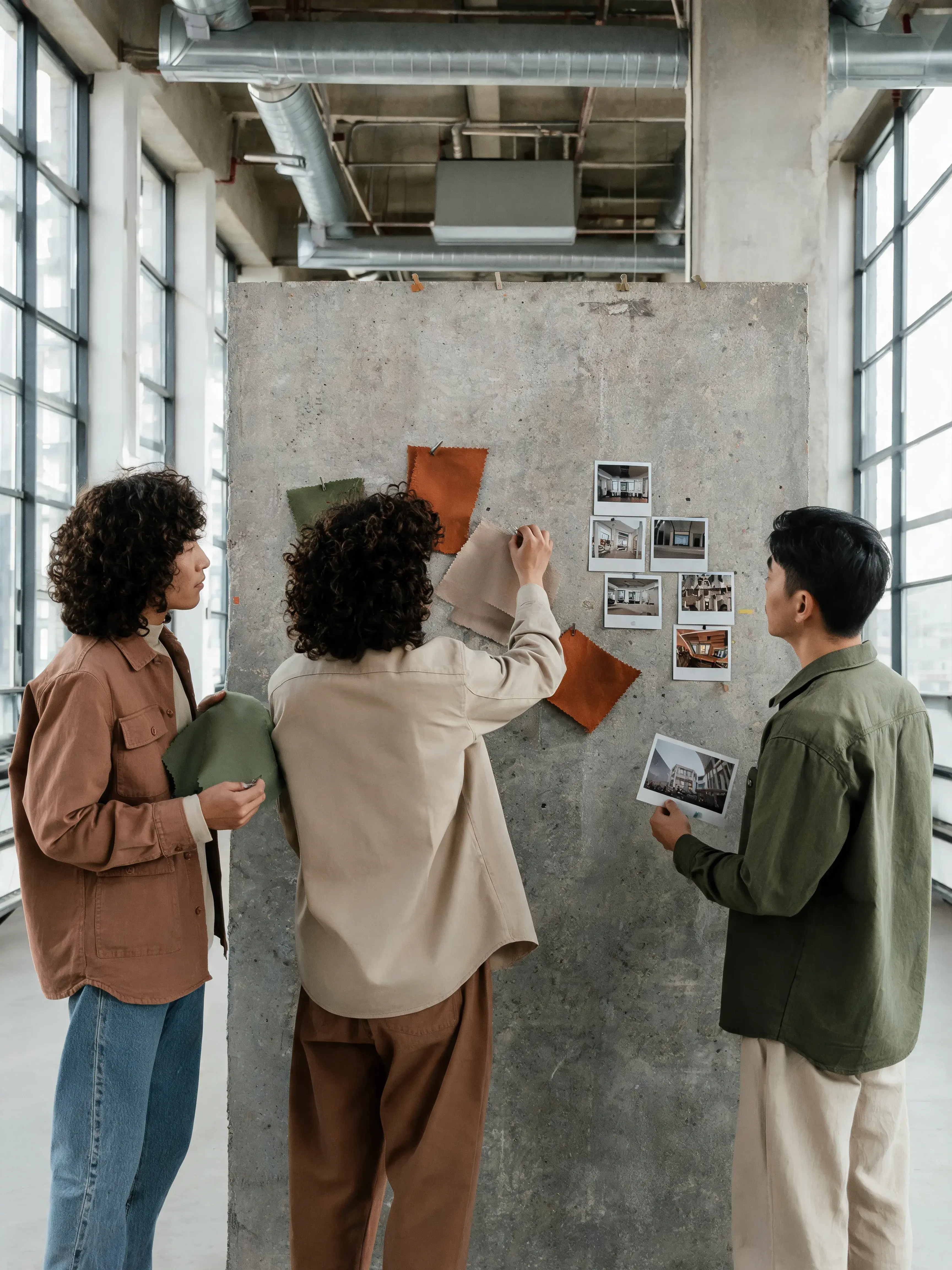 Équipe de dos construisant tableau d'inspiration – photos polaroid, tissu, mur béton, loft